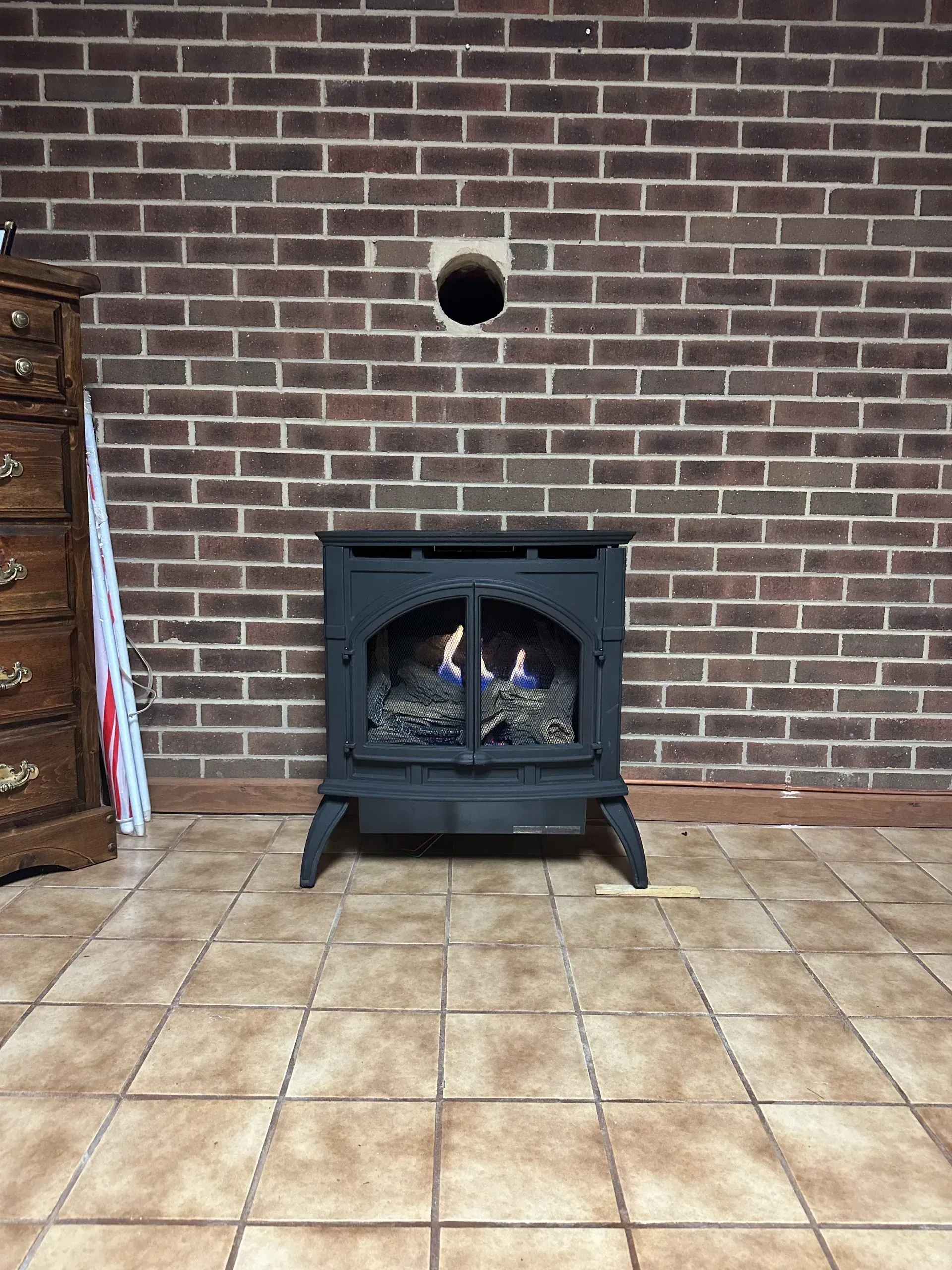 A wood stove is sitting in front of a brick wall in a room.