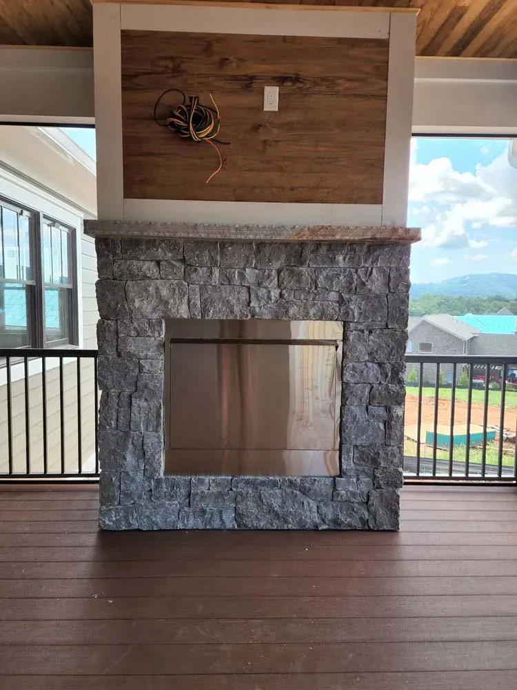 A stone fireplace with a stainless steel frame is sitting on a wooden deck.
