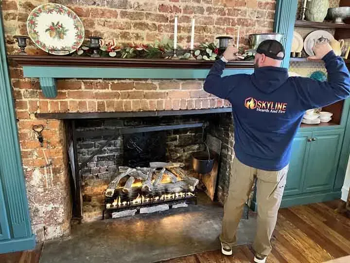 A man in a blue hoodie is standing in front of a fireplace.