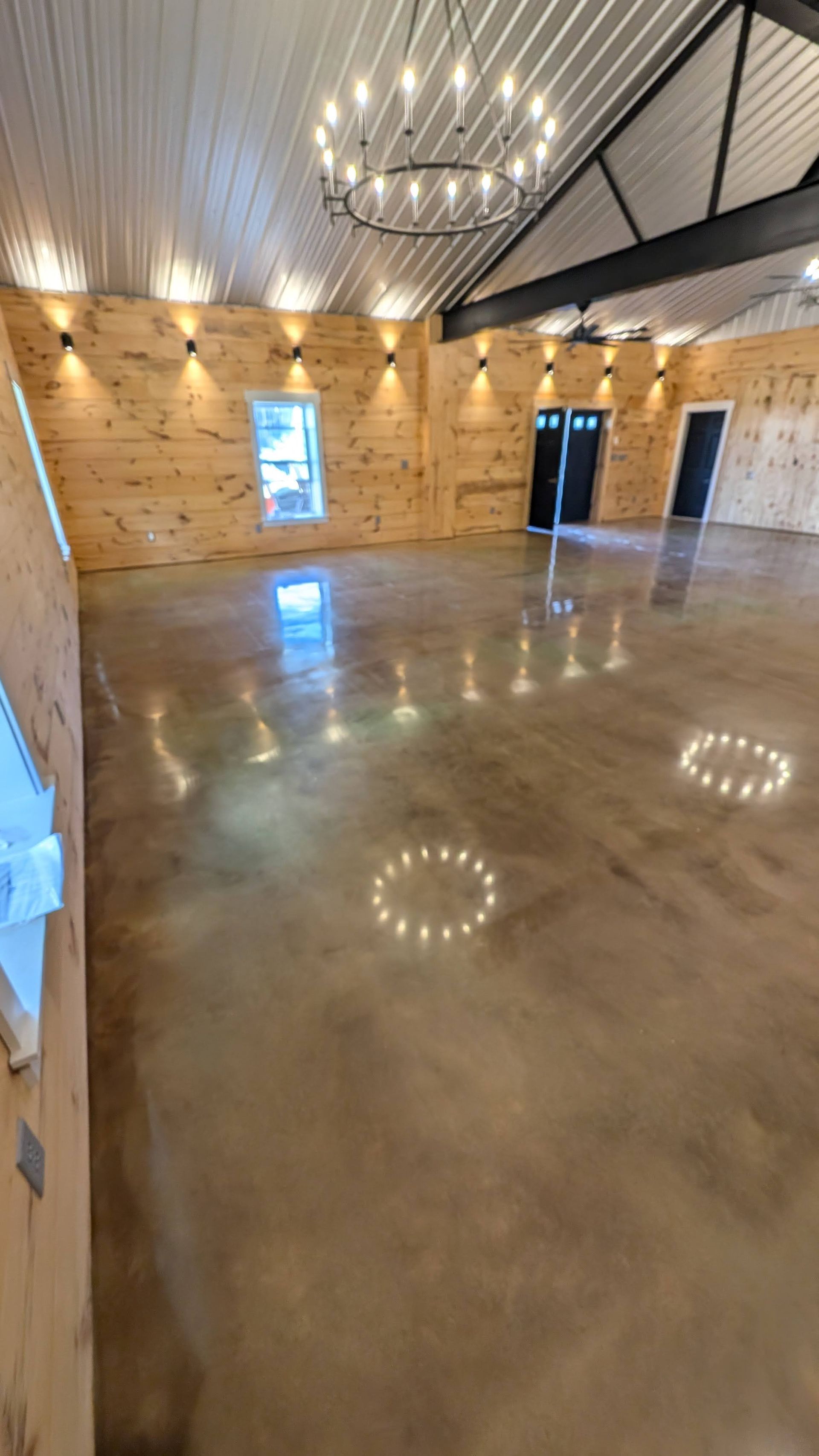 Large empty event space with polished concrete floor, wood-paneled walls, and a chandelier.