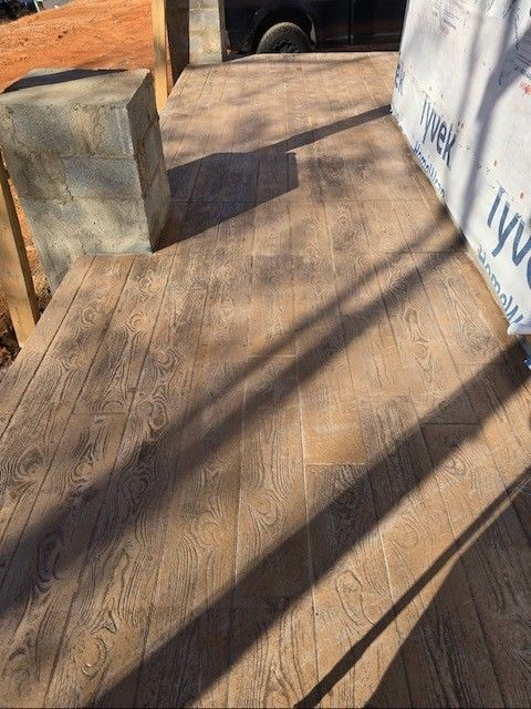 A light brown, wood-grain stamped concrete porch under construction, featuring a concrete block pillar and Tyvek wrapping.