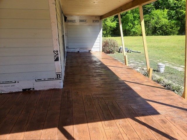 A covered porch with wood-look stamped concrete flooring alongside a house under construction.