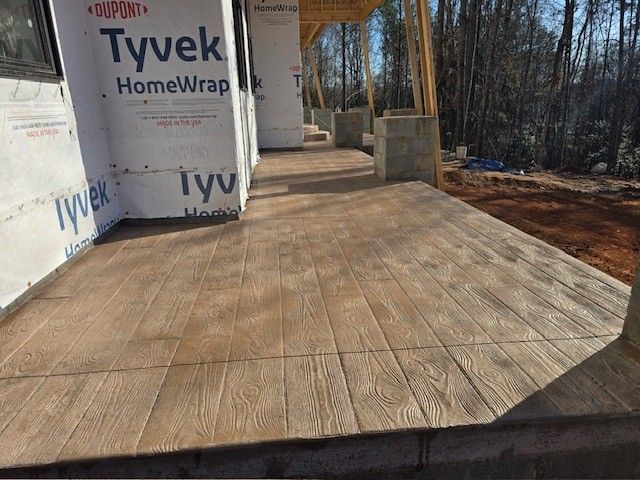 A close-up of a new concrete porch stamped to look like wooden planks, adjacent to a house under construction.