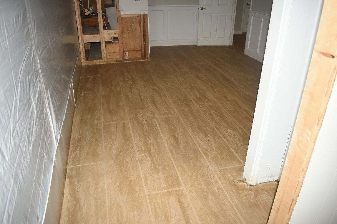 A room under renovation with wood-look flooring installed, visible wall framing, and unfinished wall sections.