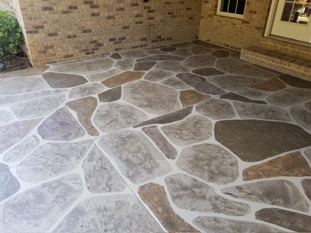 A concrete patio floor with a stamped, multi-colored flagstone pattern in shades of gray, tan, and brown.