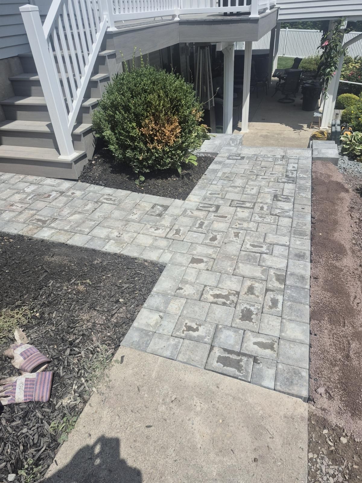 Stone walkway leading to a porch, bordered by gravel and shrubs beside a house