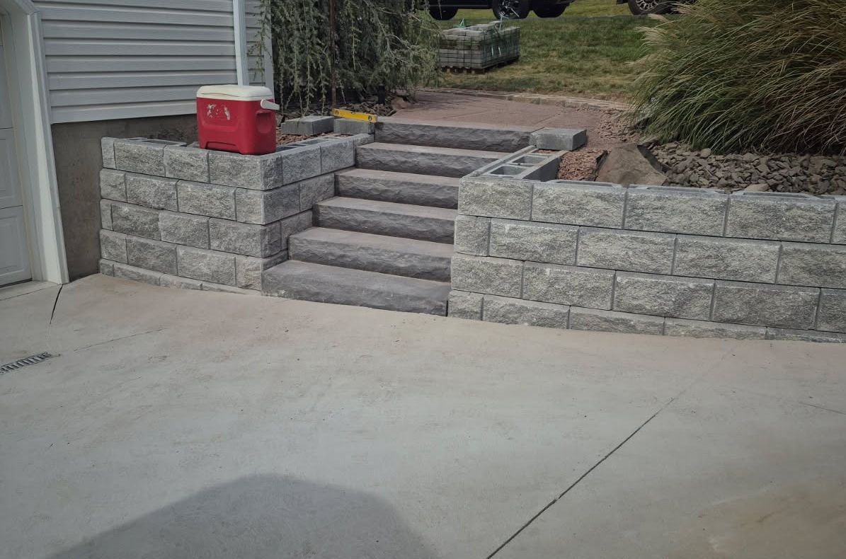 Concrete driveway with stone steps and retaining walls beside a house, with a red cooler near the top.