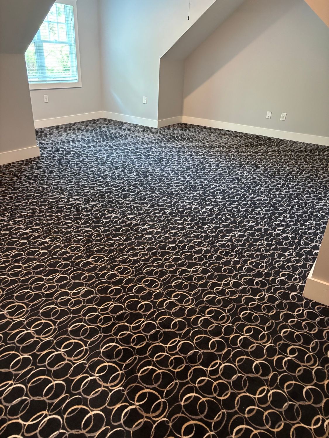 Empty room with patterned dark carpet, light gray walls, and a small window.