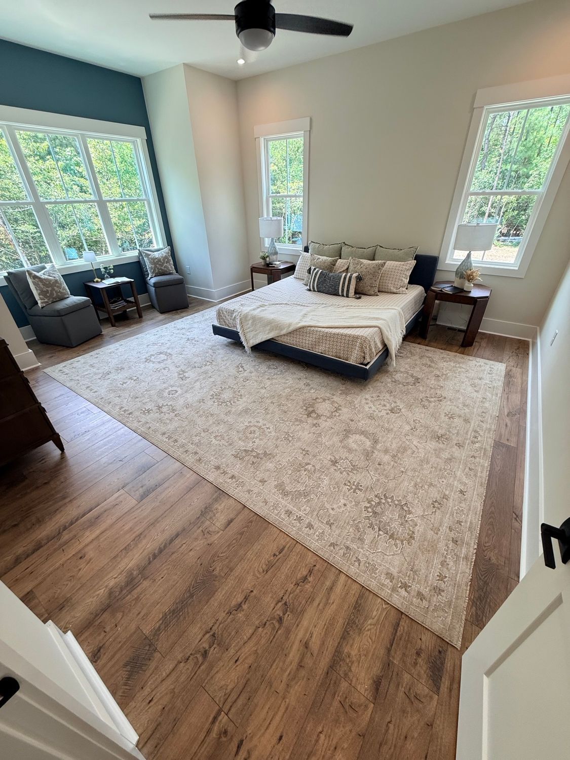 Spacious bedroom with a low bed, large windows, a beige rug, wood flooring, and a ceiling fan.
