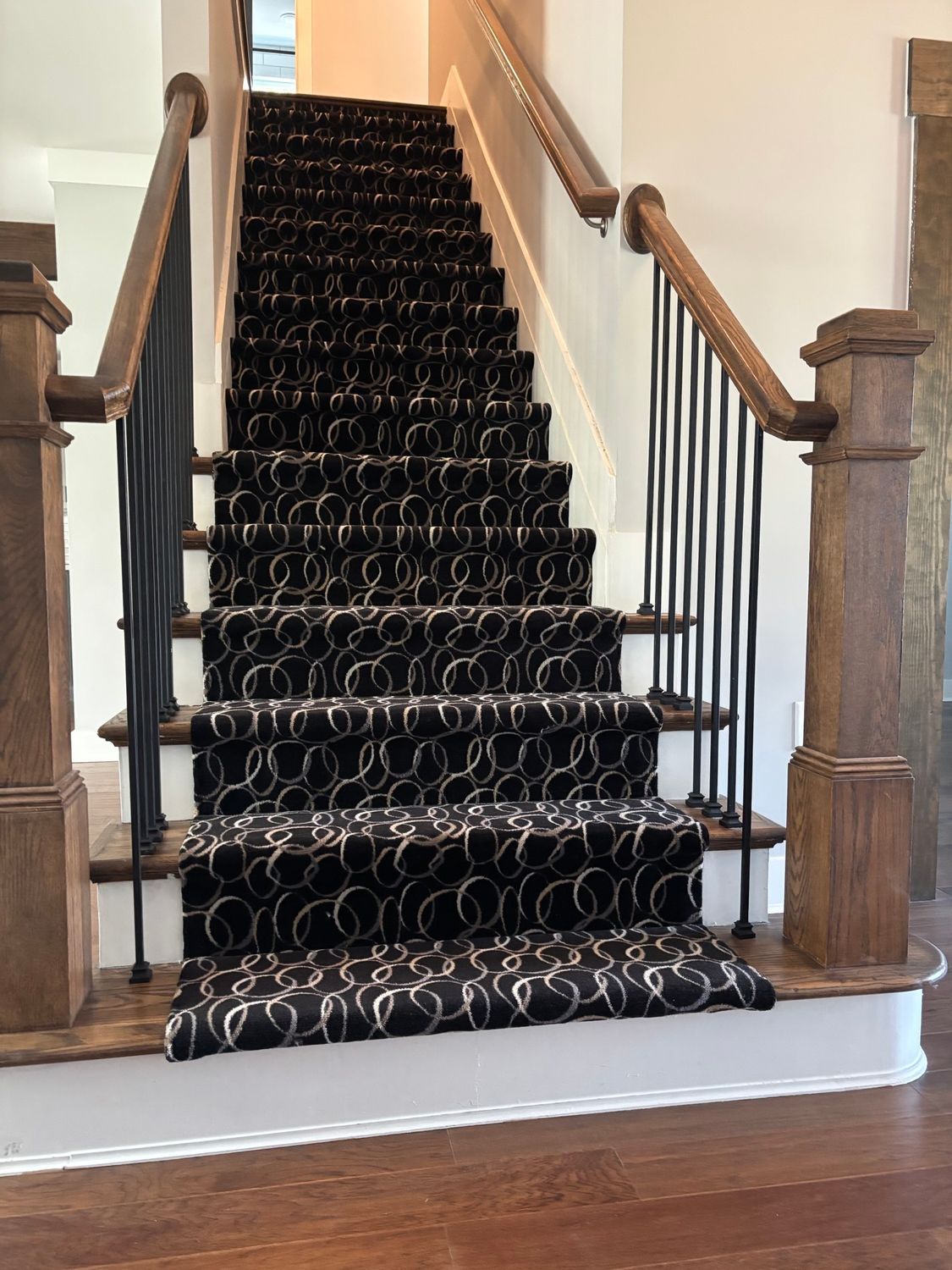 Carpeted staircase with a dark patterned runner, wooden banisters, and white walls in a home foyer