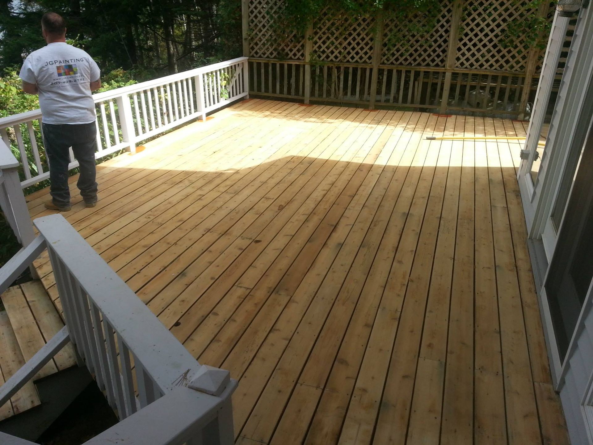 Man standing on a new wooden deck with white railing. Sunlight illuminates the deck.