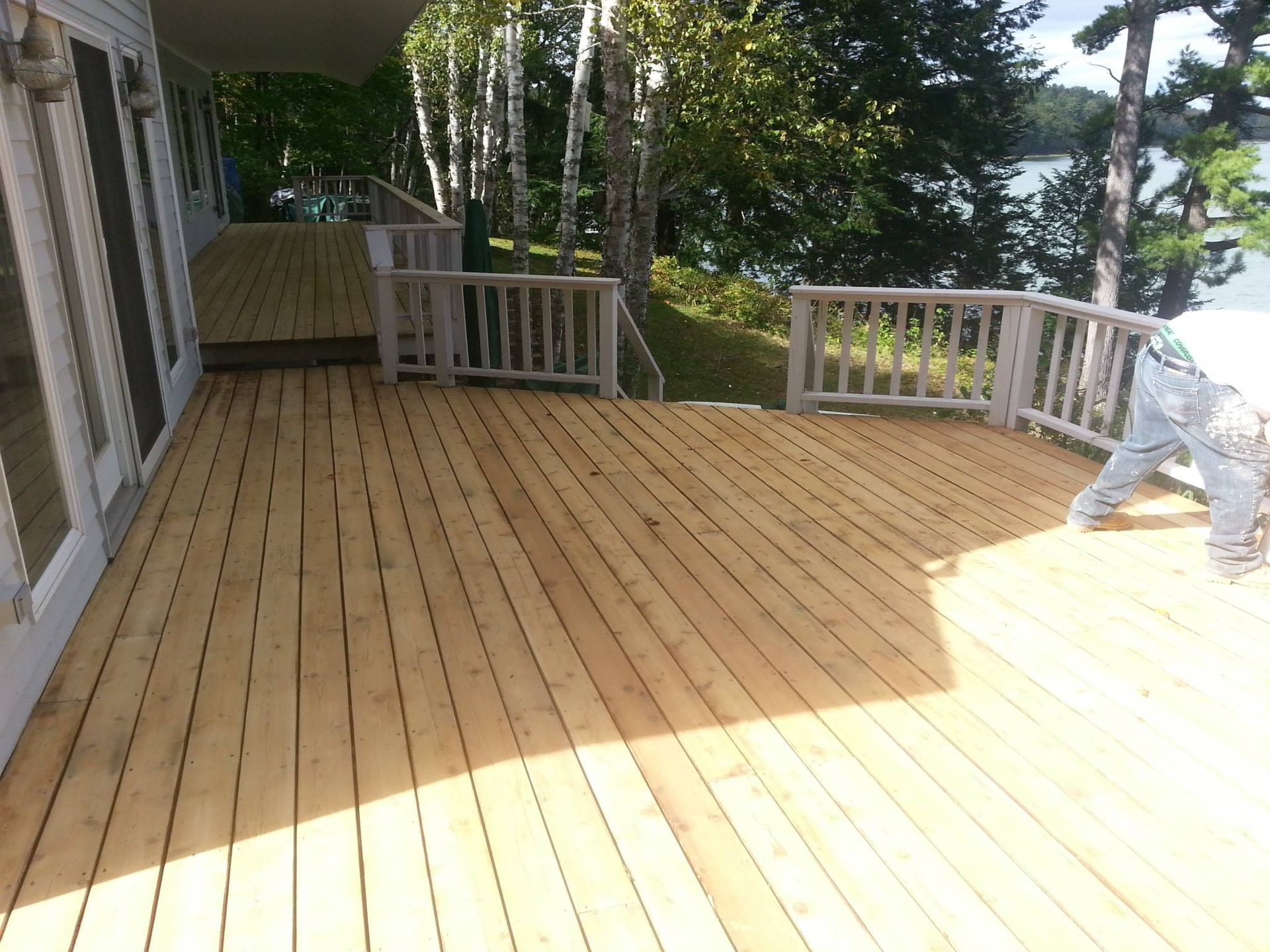 Wooden deck with railings overlooking water and trees; person working on the right.