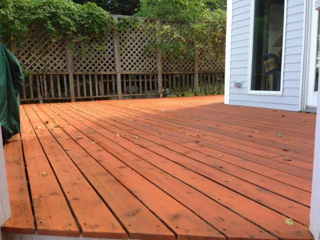 Wooden deck with orange stain in a backyard setting, next to a house.