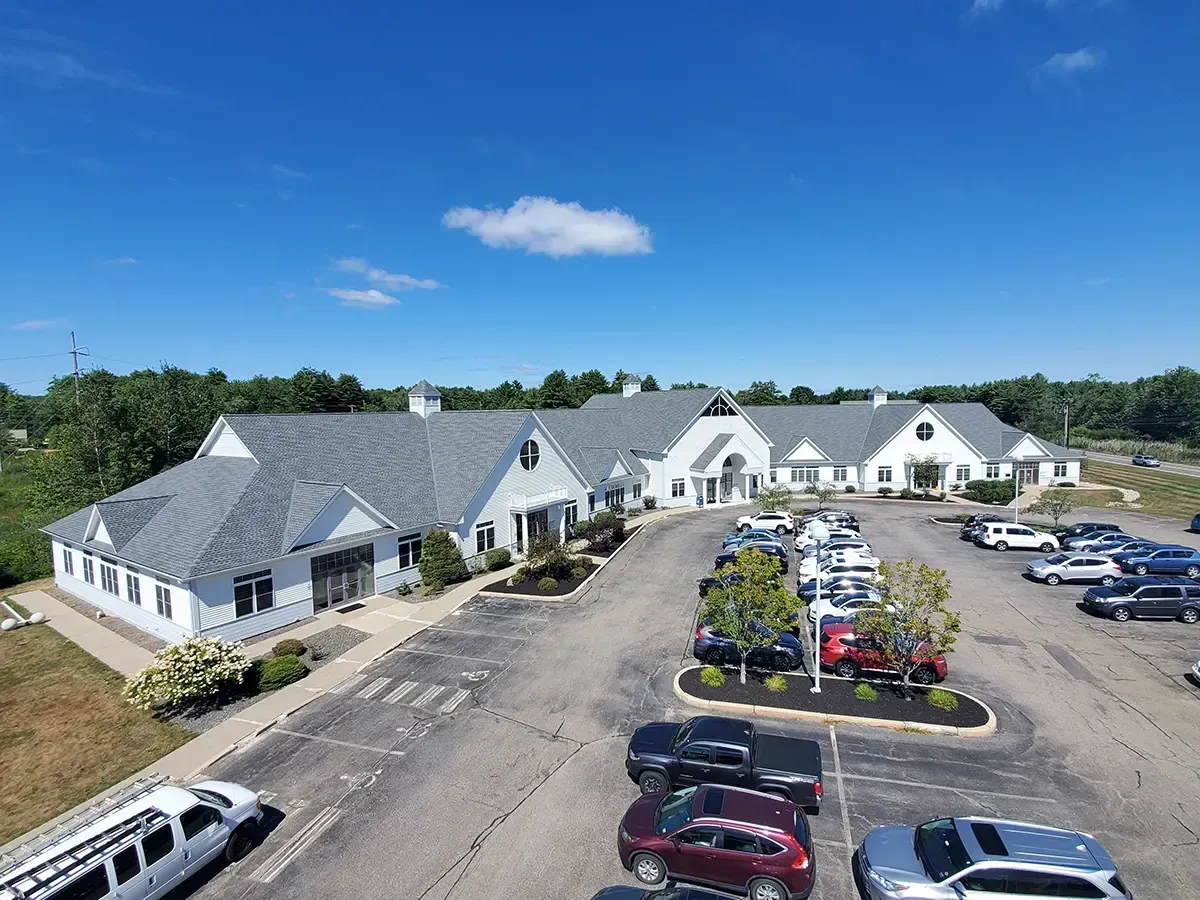 White office buildings with gray roofs, blue sky, and cars in a parking lot.