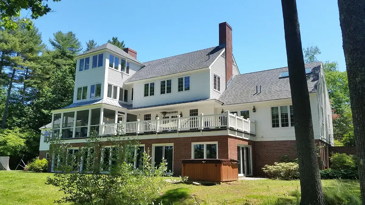 White house with red brick base, screened porch, and hot tub. Green trees and blue sky background.