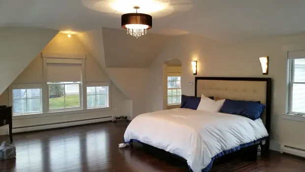 Spacious bedroom with dark wood floors, a large bed, and a chandelier; light walls and multiple windows.