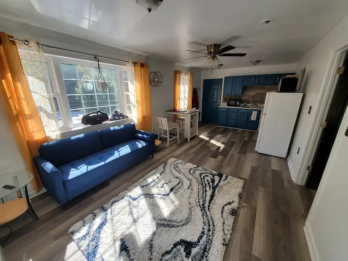 Living room with blue sofa, marble rug, dining table, and kitchen with blue cabinets.
