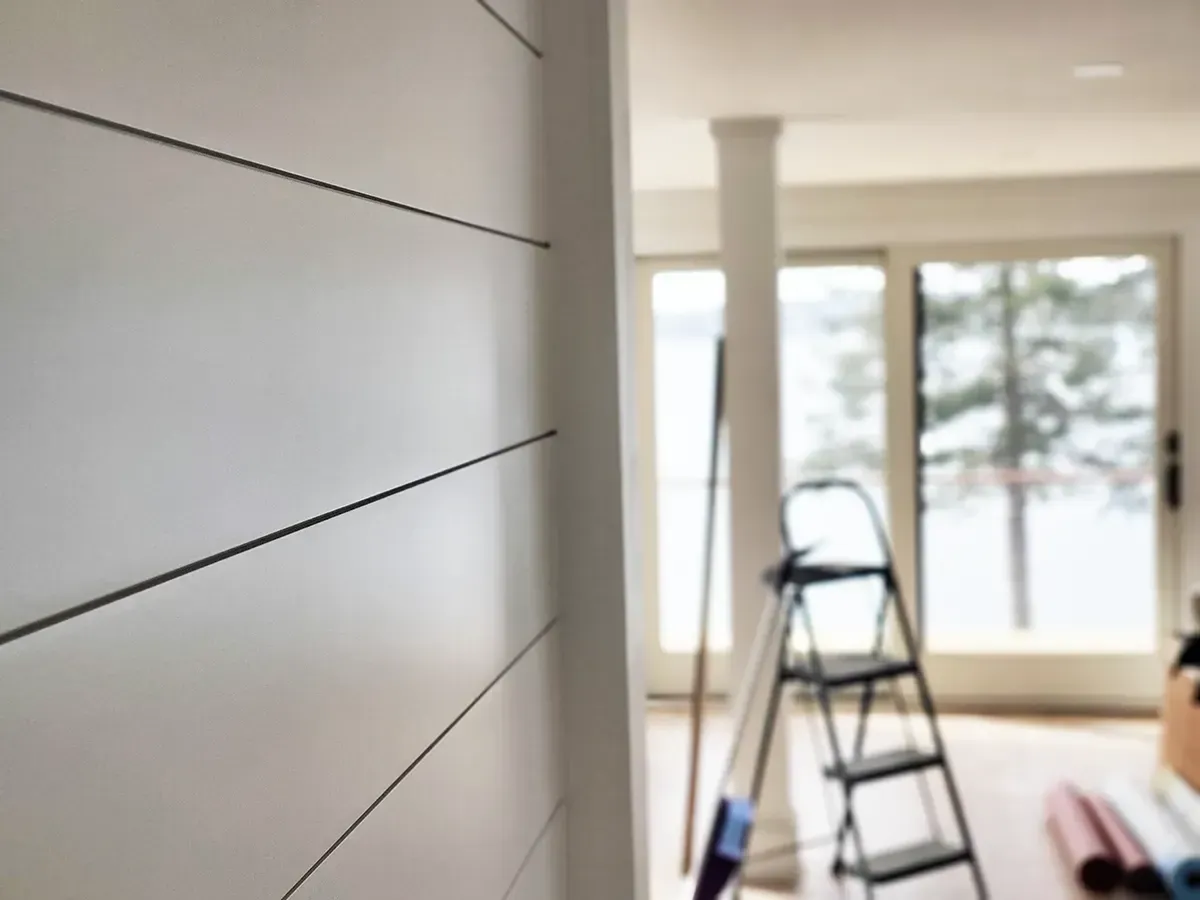 White shiplap wall in a room with a ladder, column, and sliding glass doors with an outdoor view.