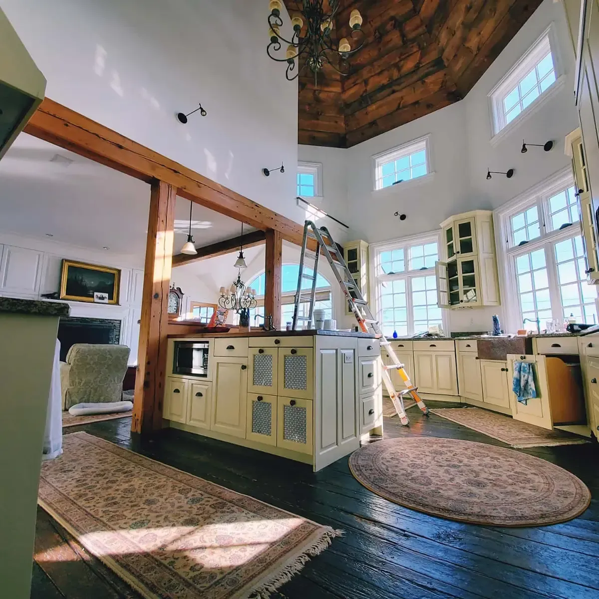 Kitchen with cream cabinets, dark wood floor, round rug, and open to living area with fireplace.