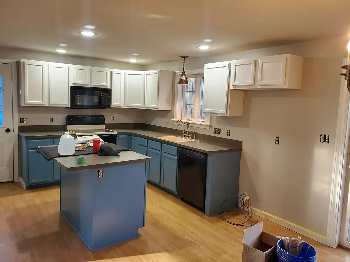 Newly renovated kitchen with blue and white cabinets, black appliances, and wooden floors.