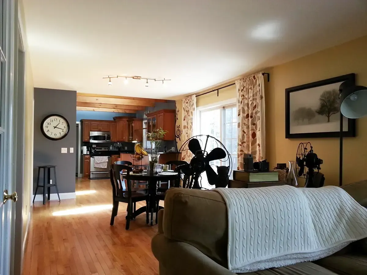 Open-concept living space with kitchen, dining area, and living room; hardwood floors, fan, curtains, and a clock.