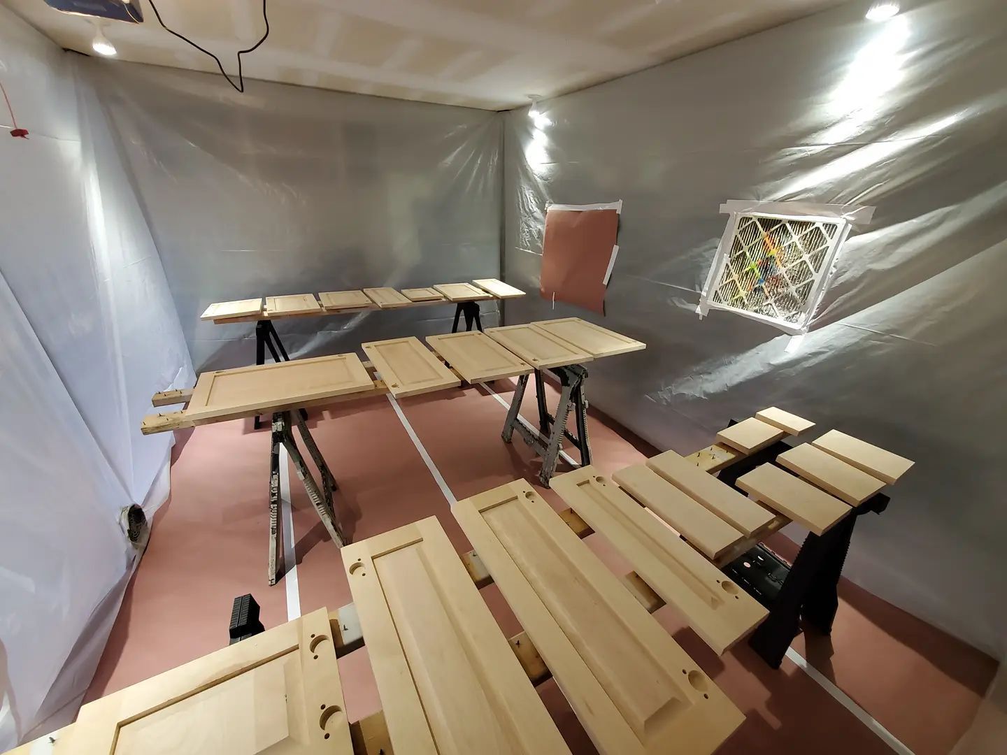 Spray paint booth with wood cabinet doors on sawhorses, covered in plastic sheeting.