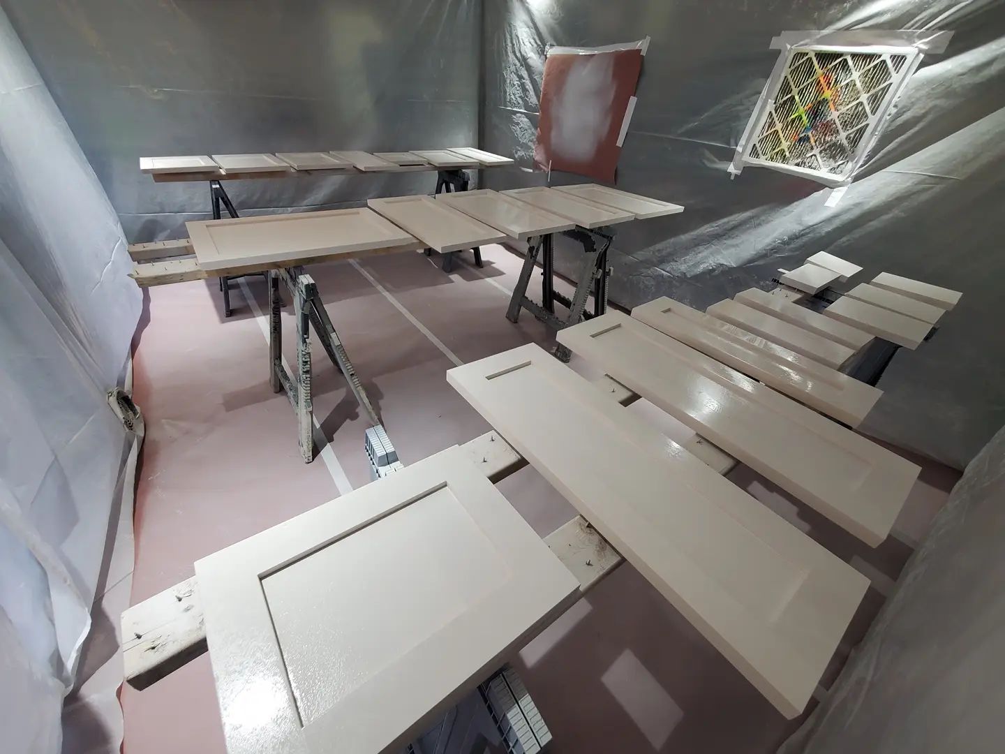 Cabinet doors and drawers are drying in a paint booth after being sprayed with a light beige paint.
