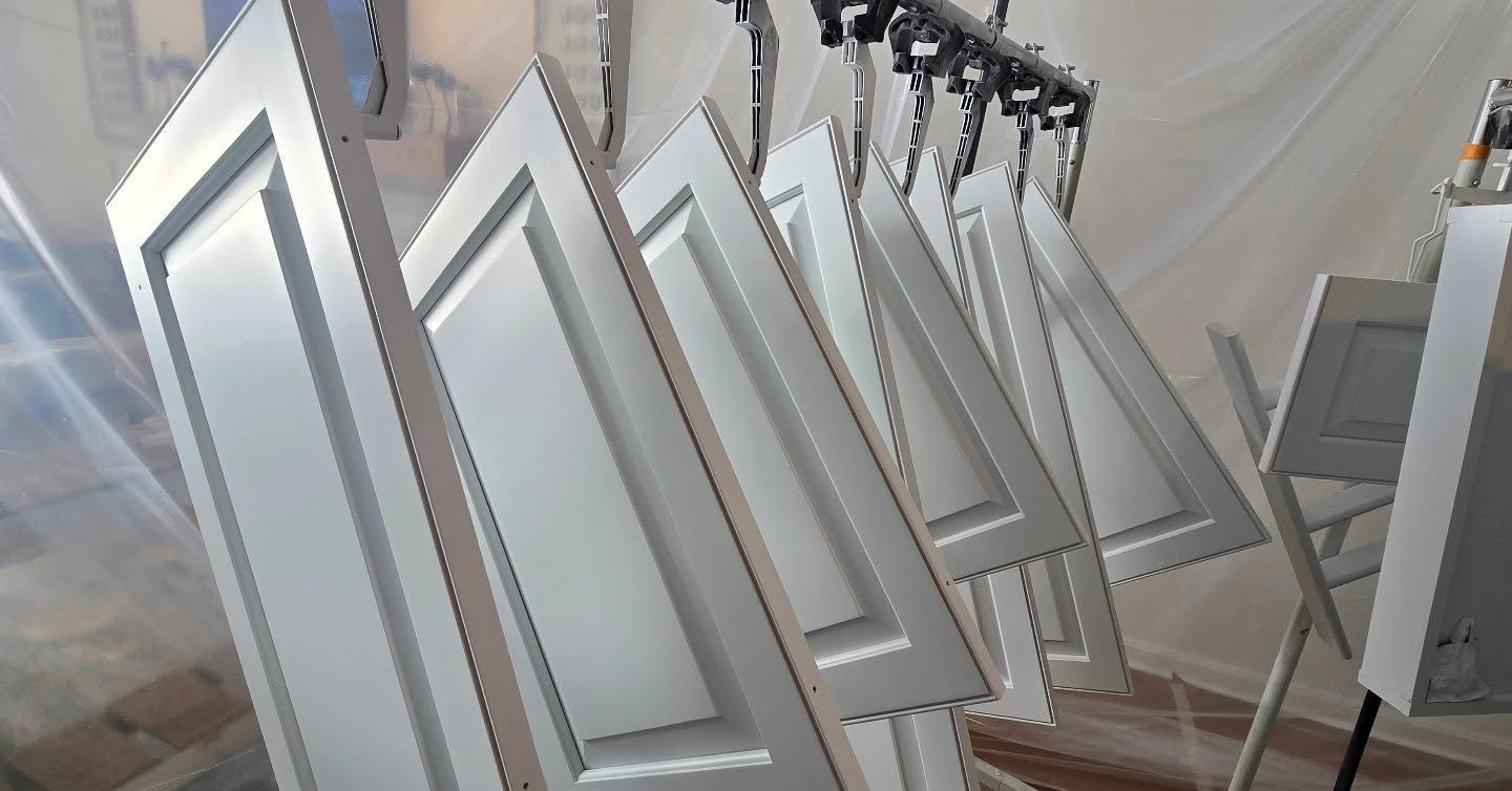 White cabinet doors hanging from a rack, being painted in a spray booth.