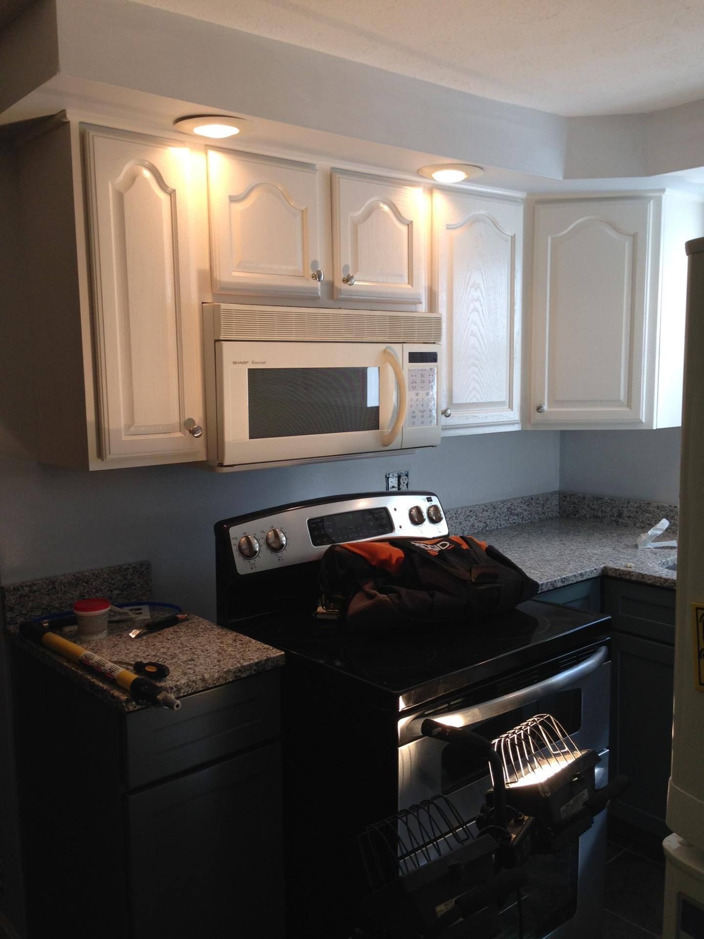 White kitchen cabinets, microwave above black stovetop, granite countertops.