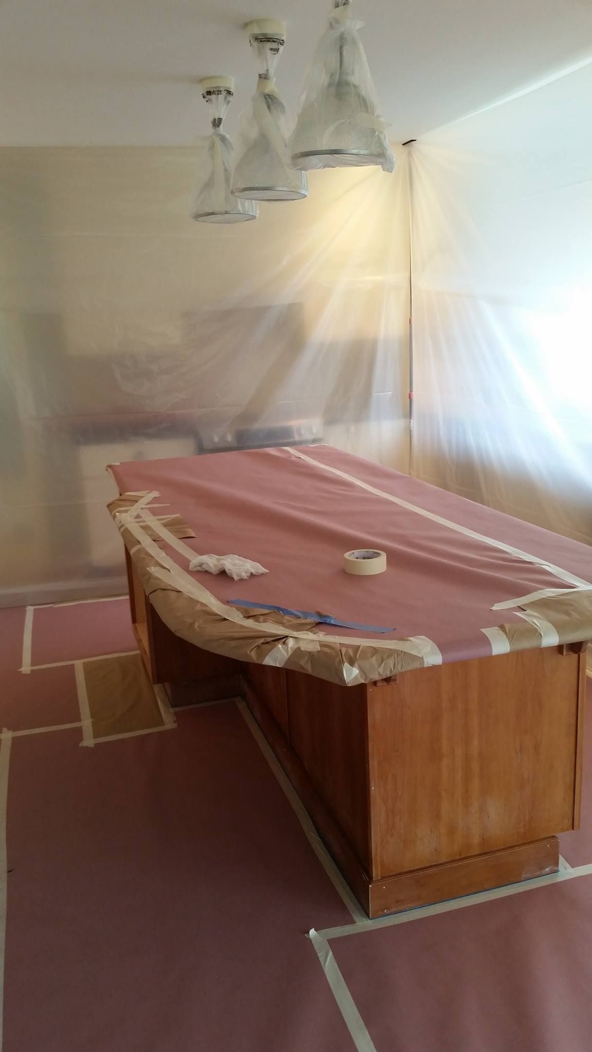 Office room prepared for painting, furniture covered, lights masked, floor and walls protected with plastic.