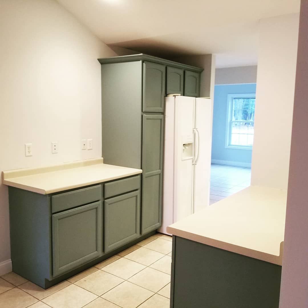 Kitchen with sage green cabinets, light countertops, and white refrigerator.