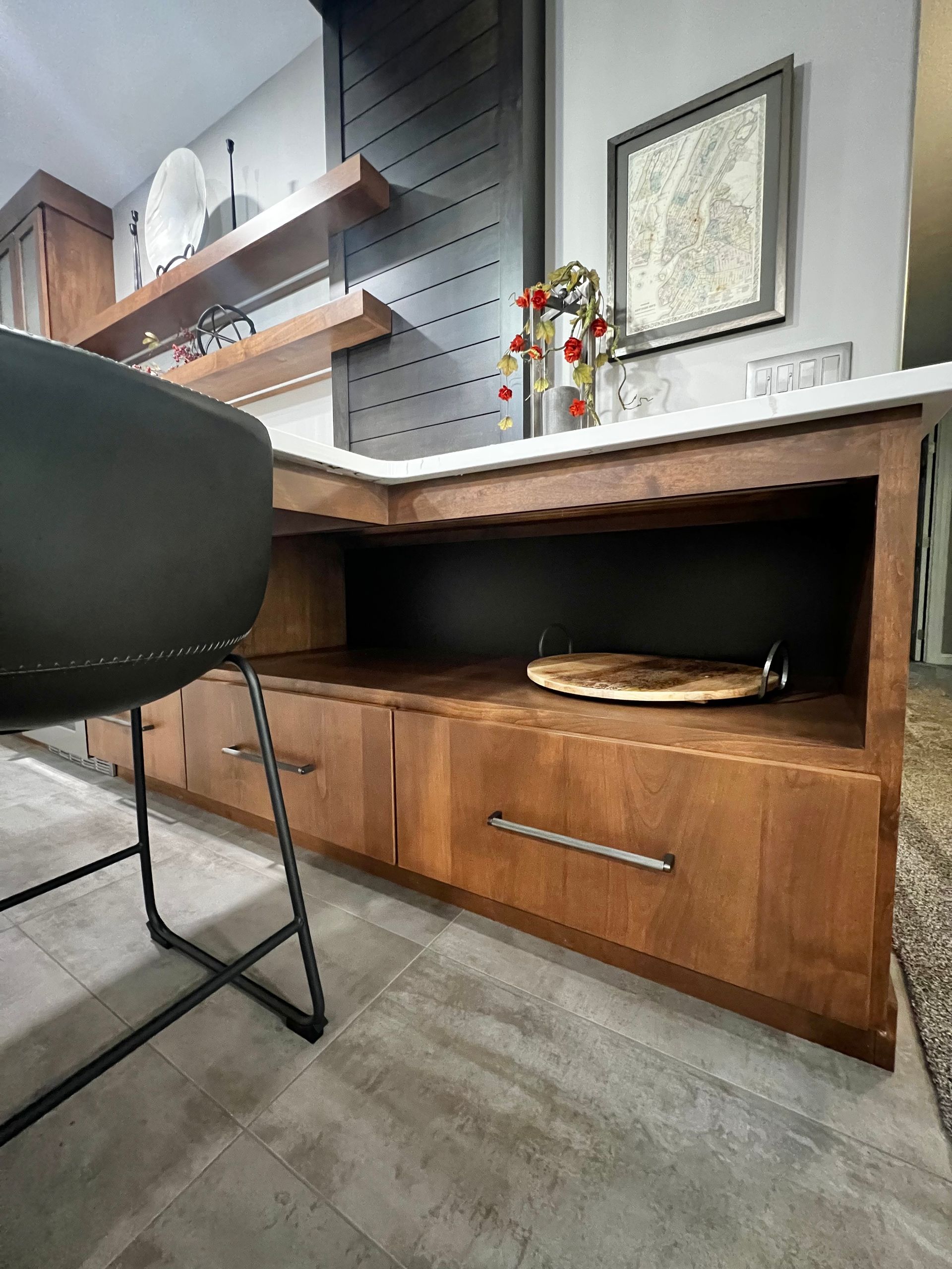 A modern wood kitchen island with two drawers, a lower open shelf, and a black paneled wall behind it.