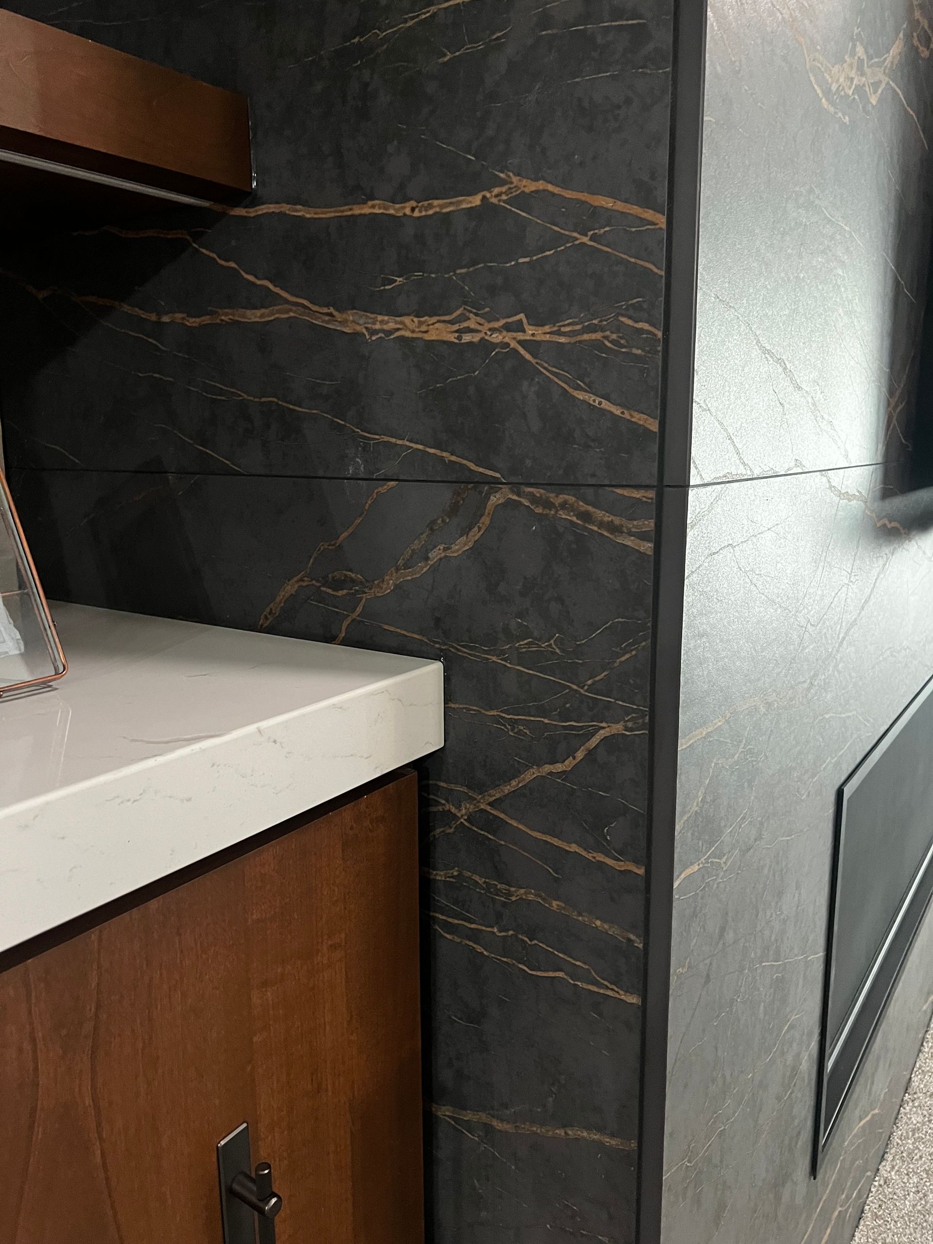 Close-up of a dark, gold-veined stone fireplace wall next to a wooden cabinet with a light-colored countertop.