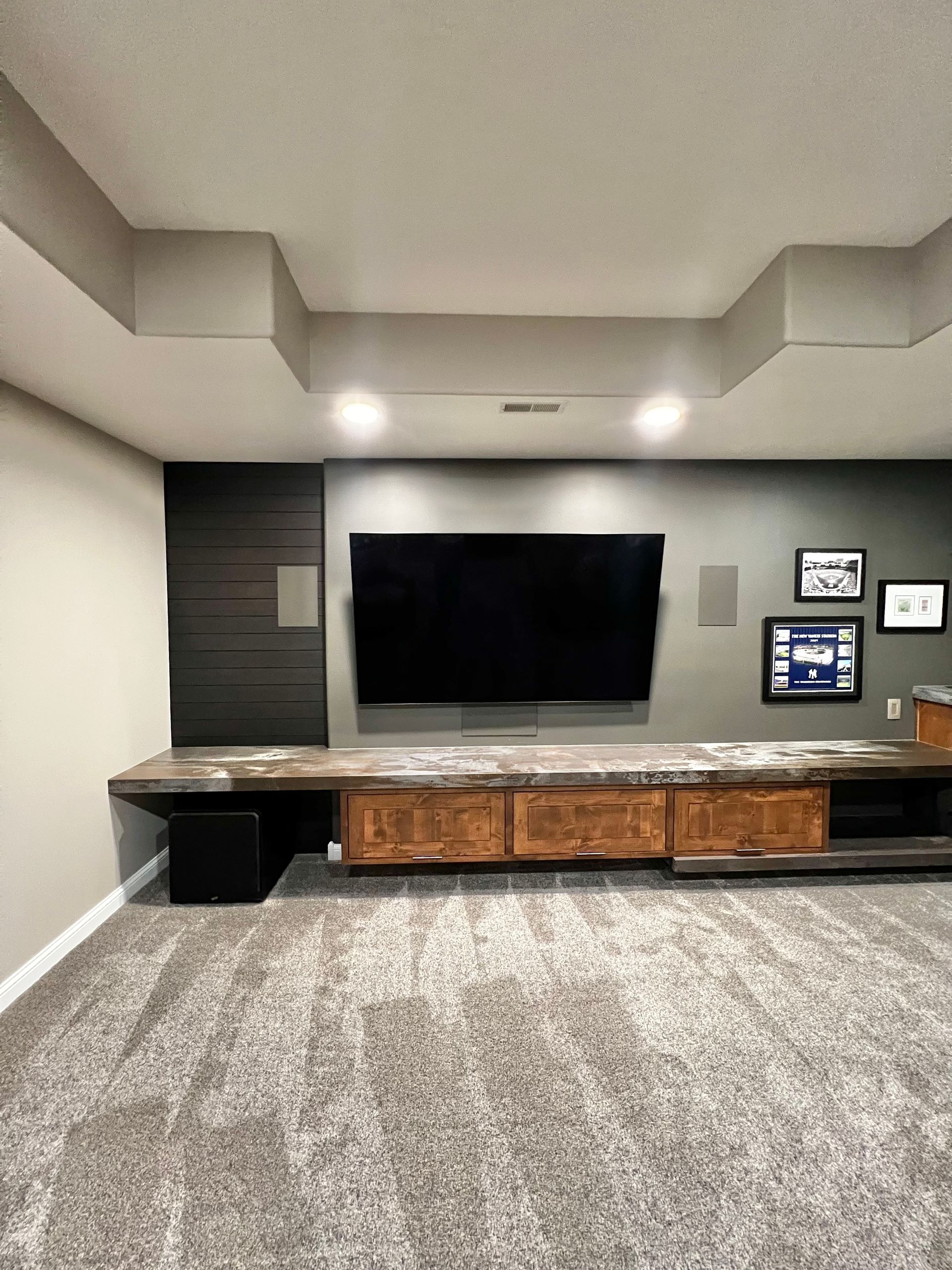 A media wall features a mounted TV, a long marble-topped wooden console, dark horizontal wood accents, and framed photos.