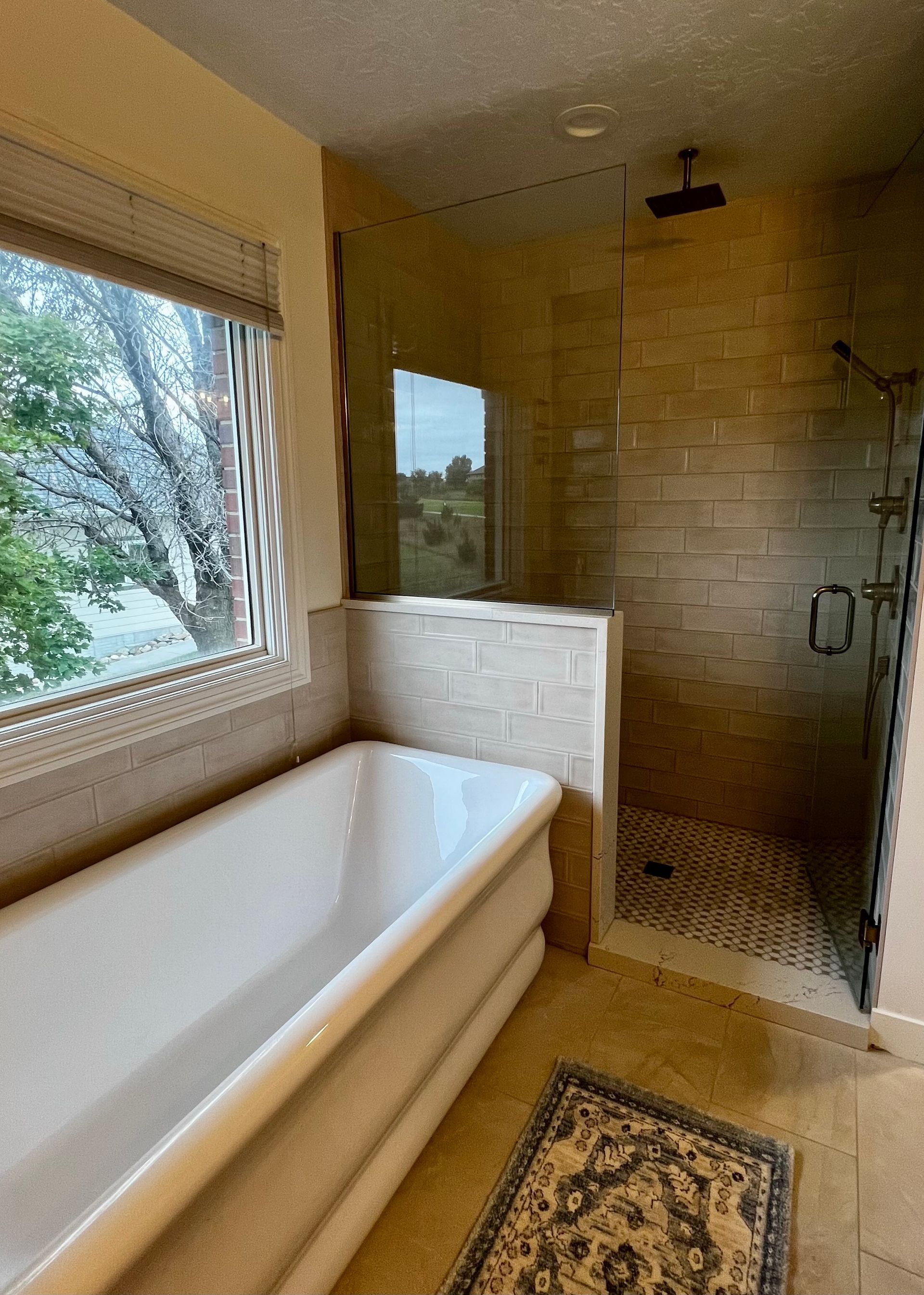 A bathroom featuring a freestanding white tub next to a walk-in shower with stone walls and a glass partition.