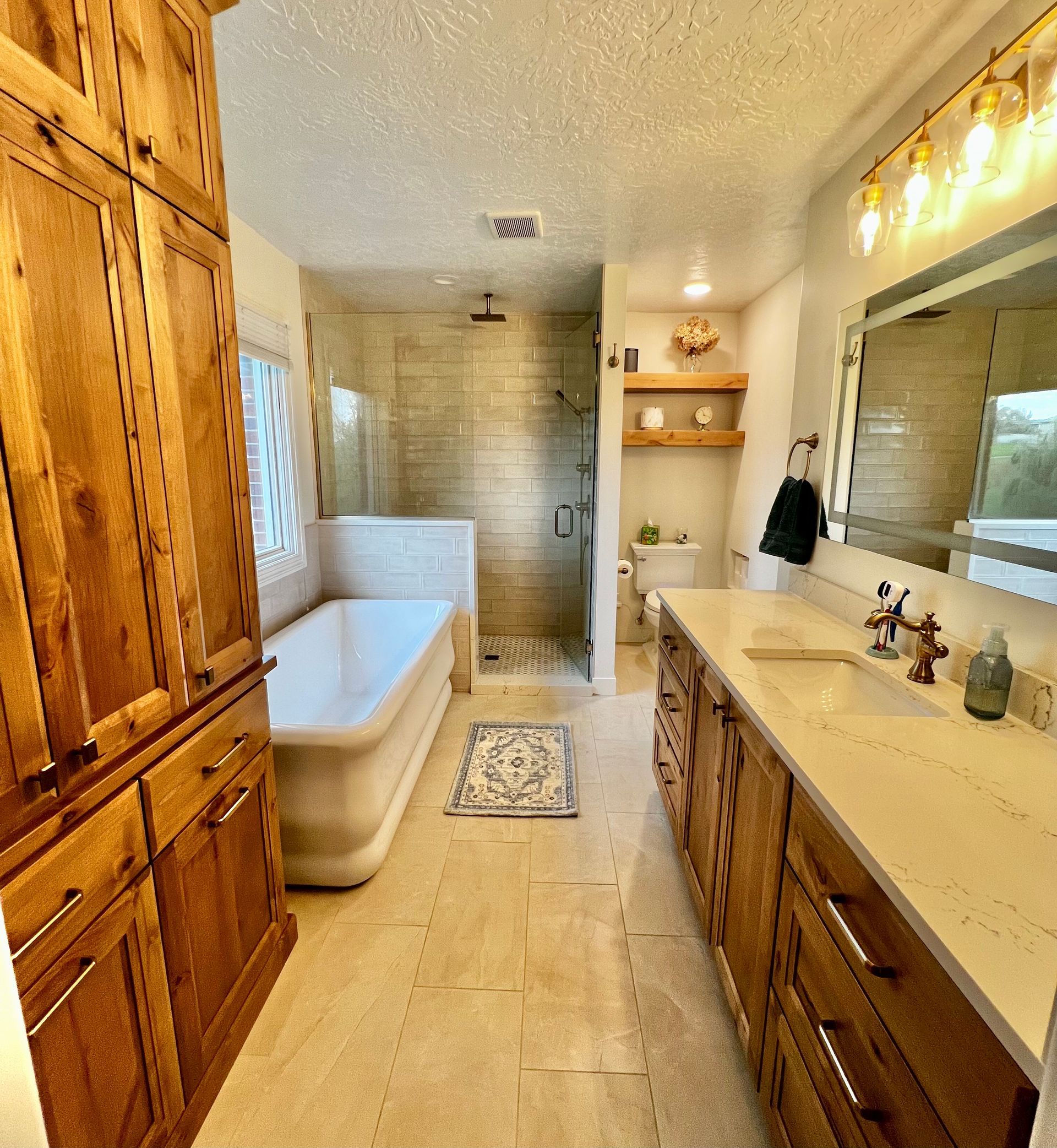 A bright bathroom with wooden cabinets, a white bathtub, a glass-enclosed shower, and a light-colored vanity.