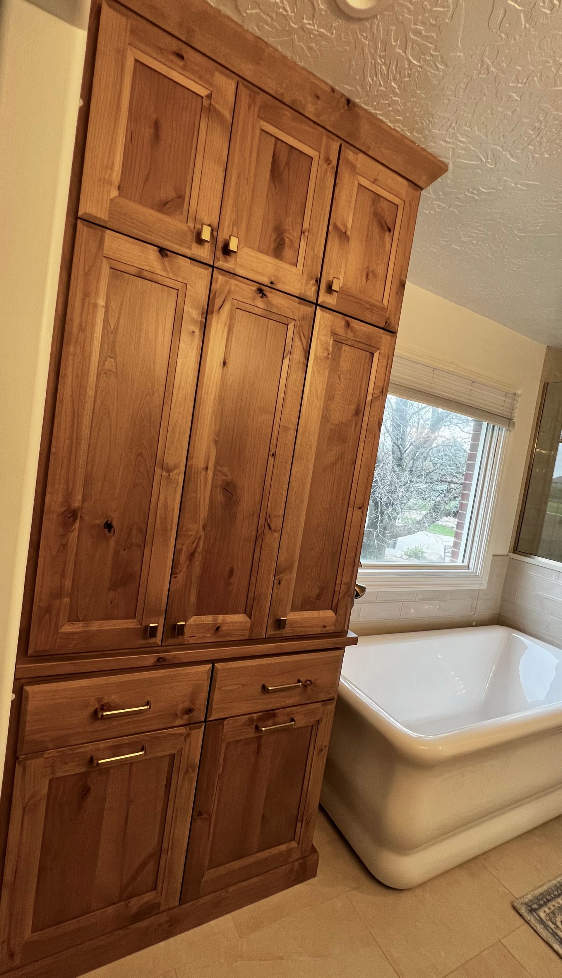 A tall, wooden storage cabinet with drawers and cupboards stands next to a white bathtub in a bathroom.