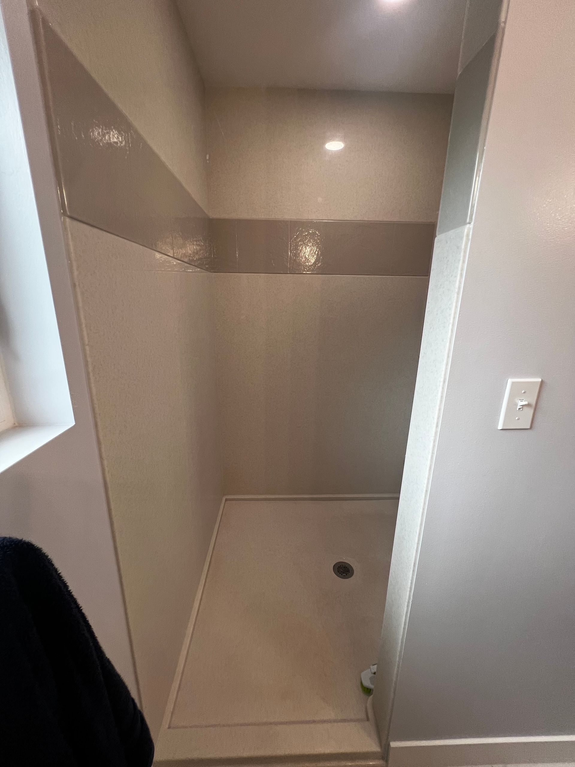 A walk-in shower with light, speckled walls, a wide horizontal accent stripe, and a floor-level drain.