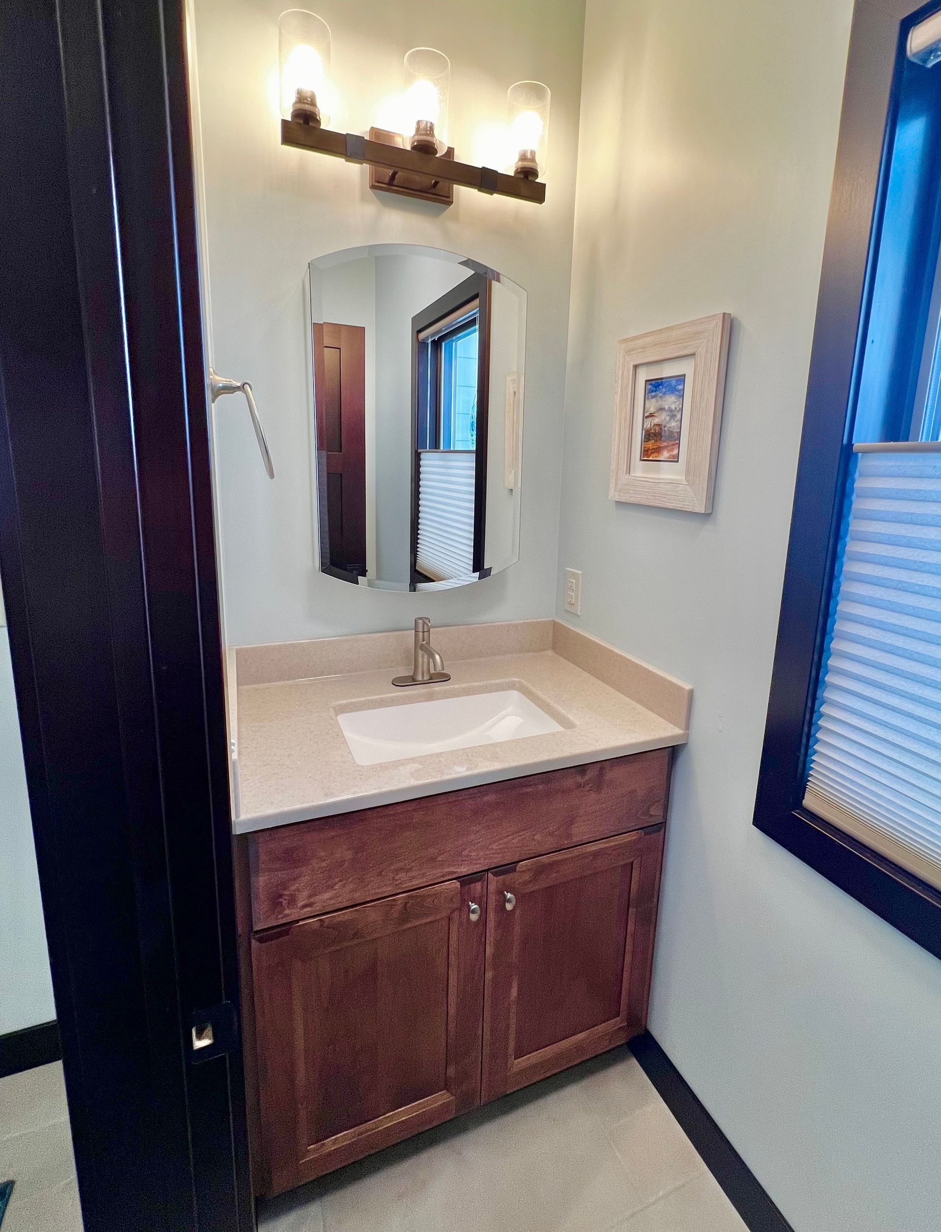A modern bathroom vanity with a wood cabinet, white countertop, sink, arched mirror, and a three-light fixture overhead.