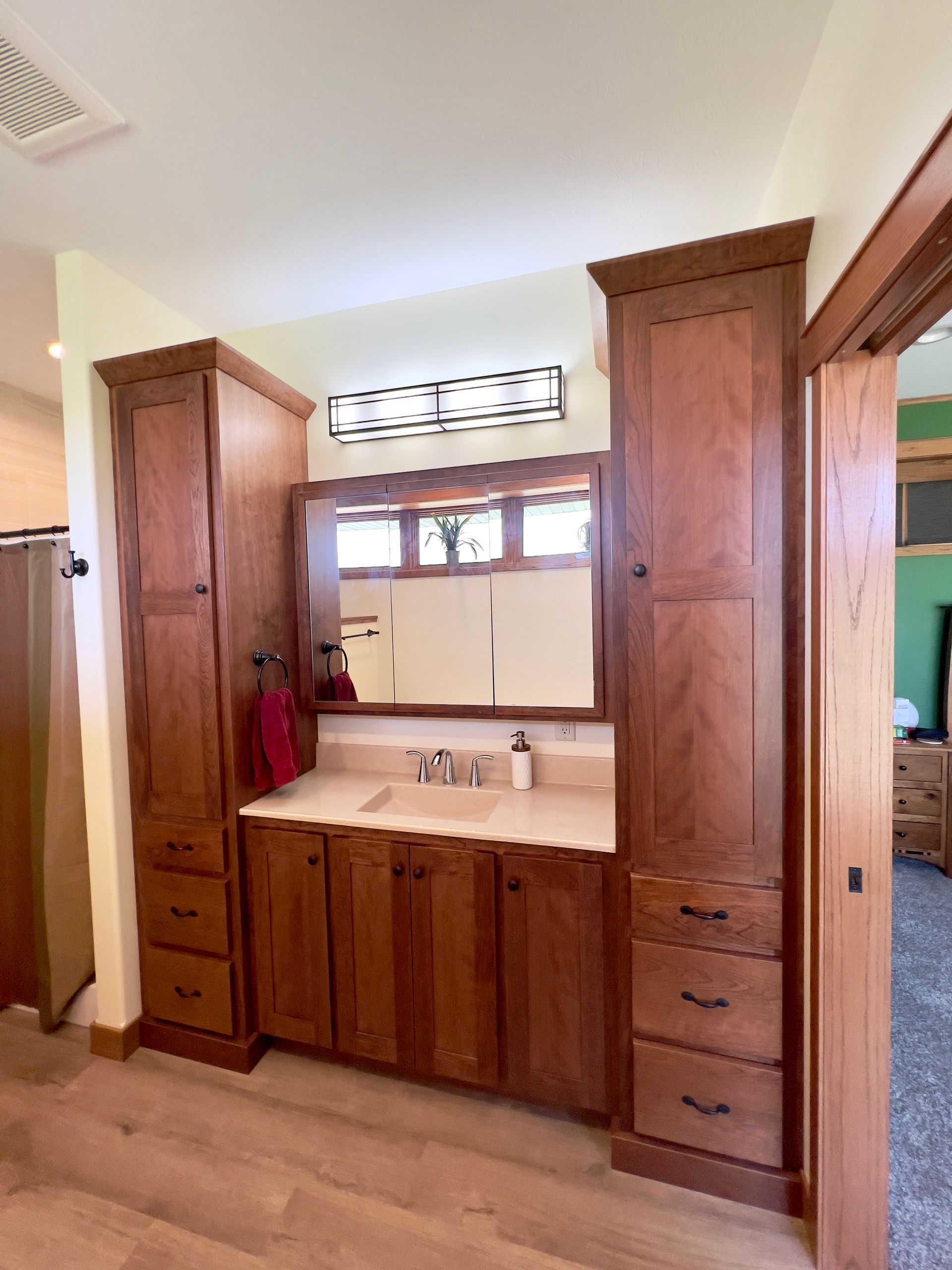 A bathroom vanity with a central sink, mirror, and two tall flanking wooden cabinetry towers on light flooring.