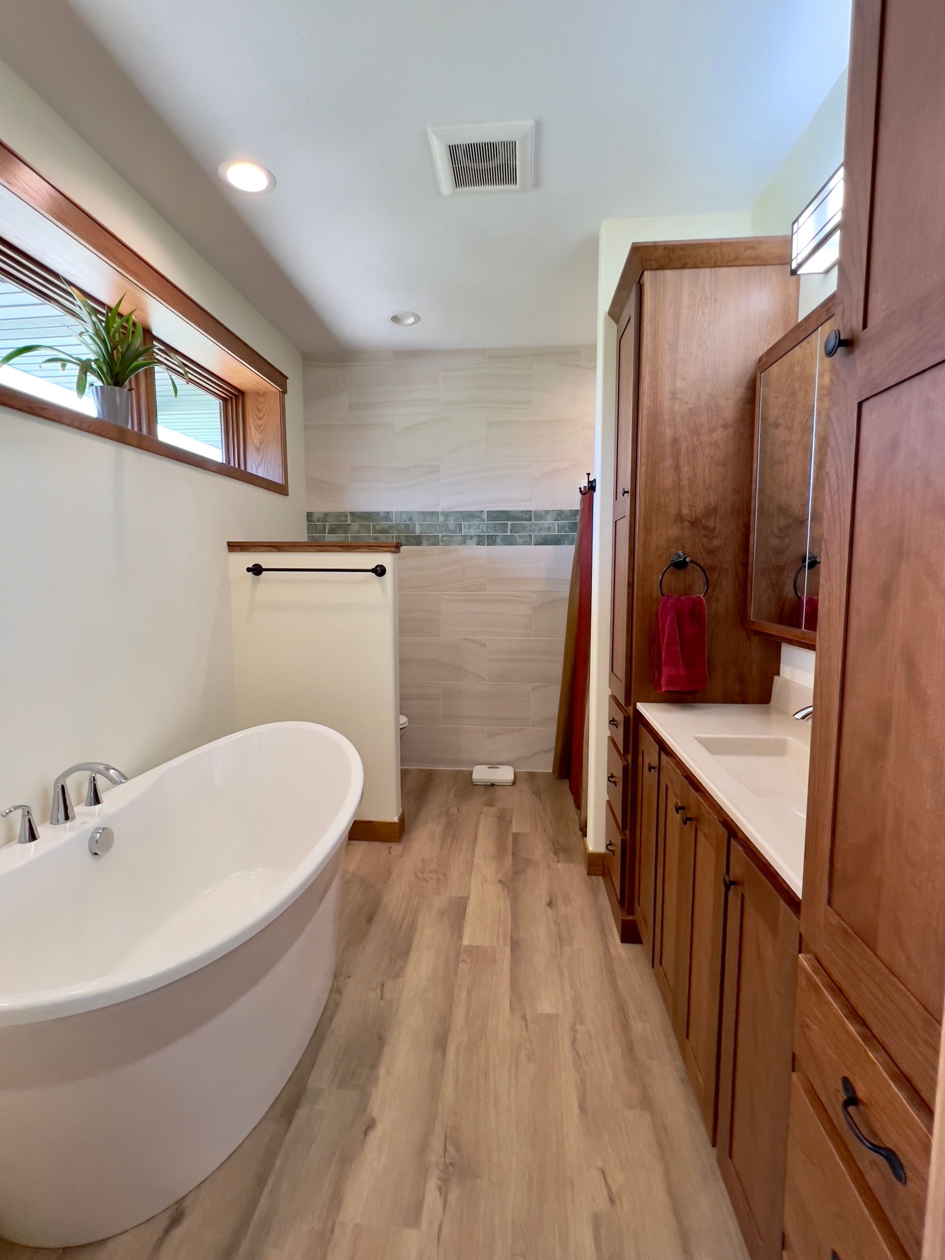 A modern bathroom with a freestanding white tub, wooden vanity, and a glass-enclosed shower against a light-toned wall.