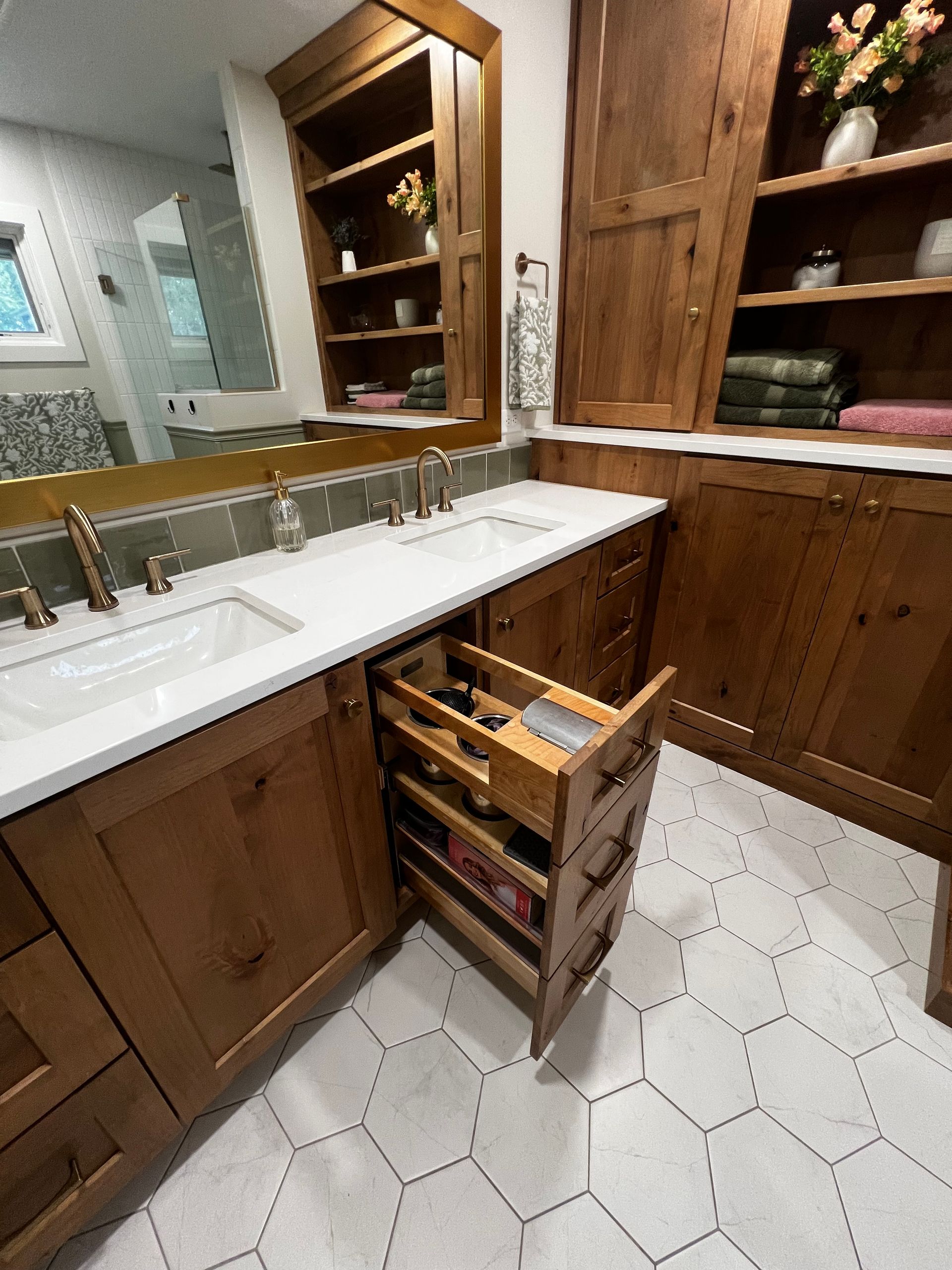 A wooden bathroom vanity with white countertops, hexagonal floor tiles, and an open pull-out drawer showing toiletries.