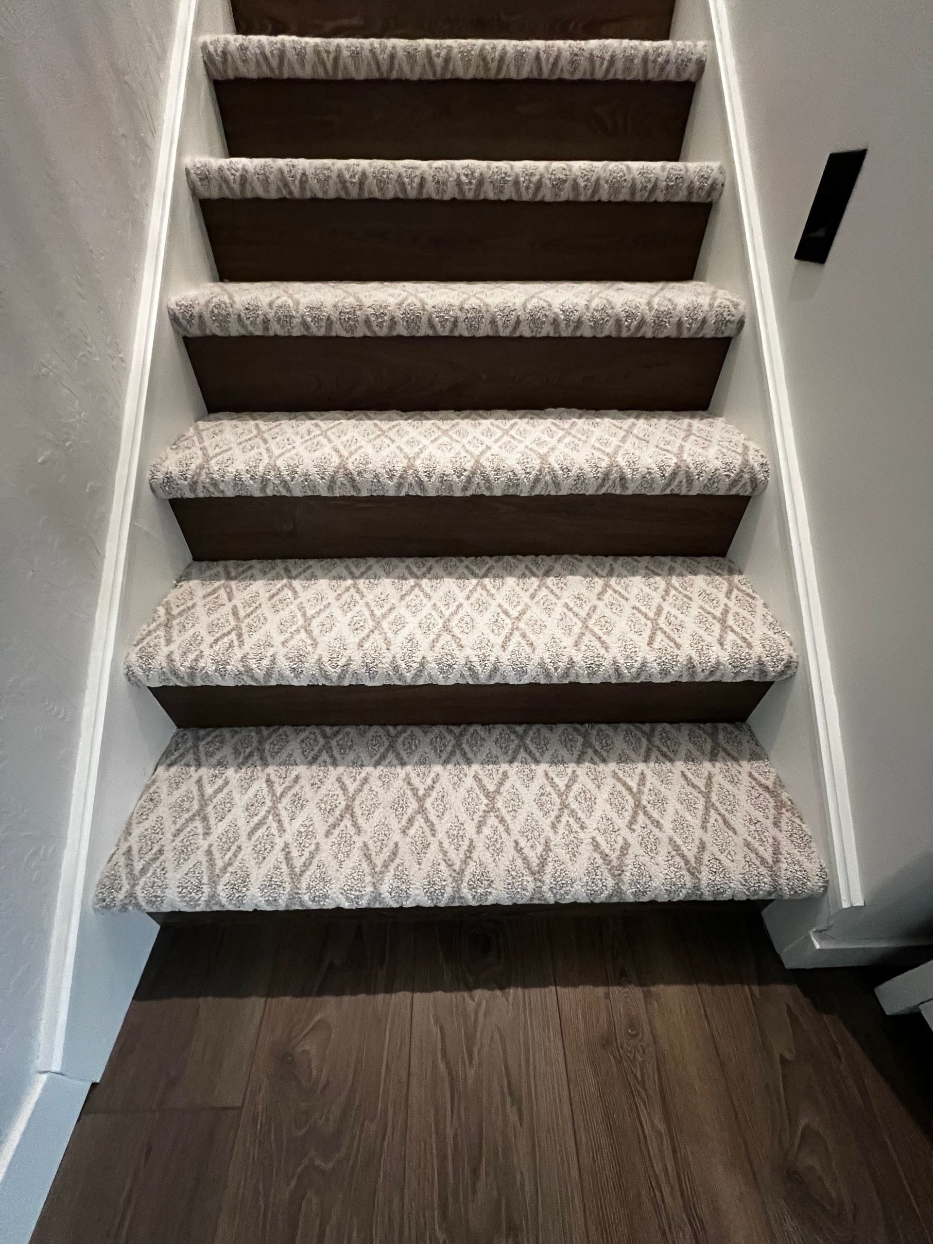 A straight staircase with dark wood treads, white risers, and a patterned light-colored carpet runner.