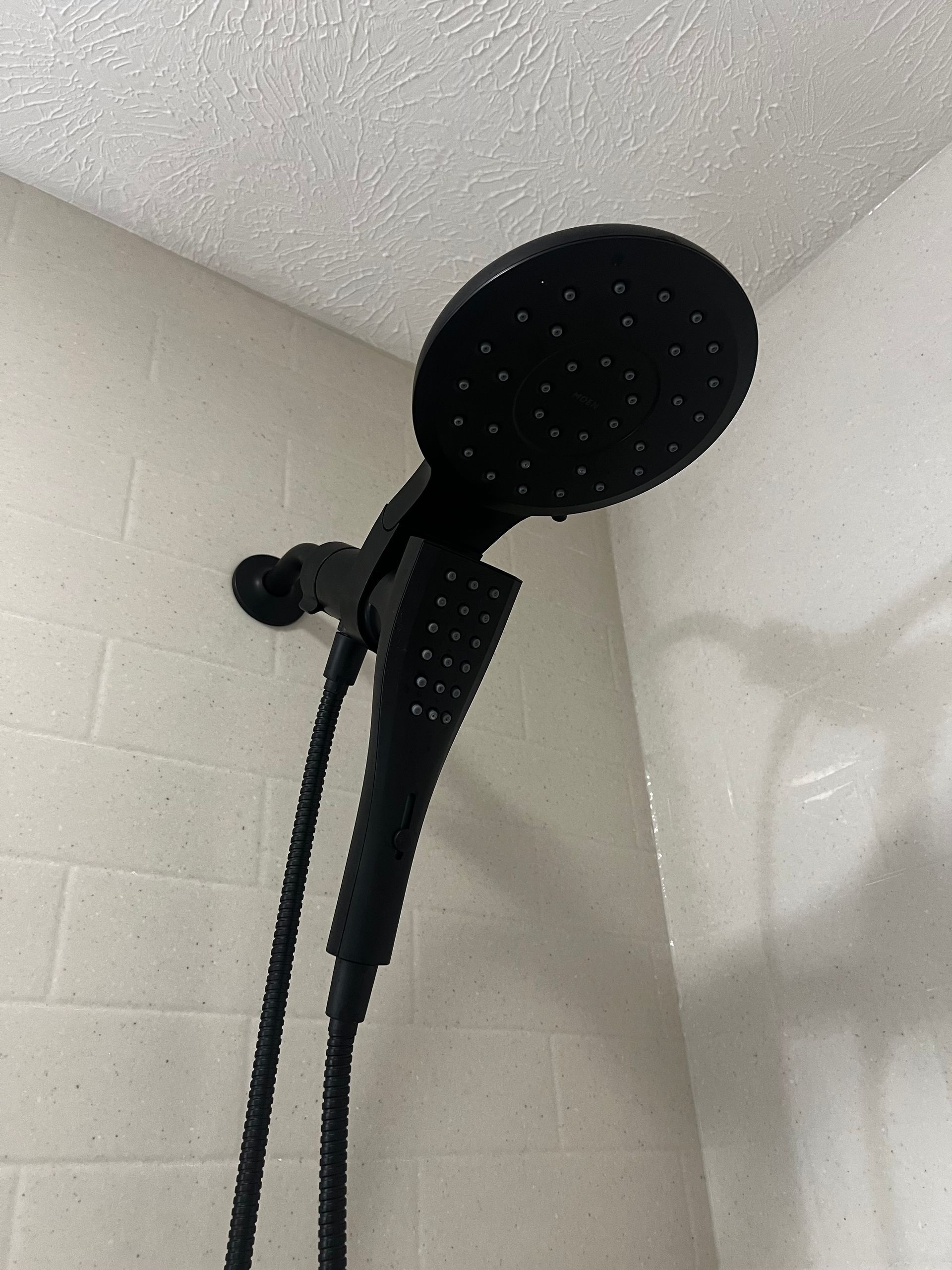 A black dual shower head assembly mounted on a white tiled wall.