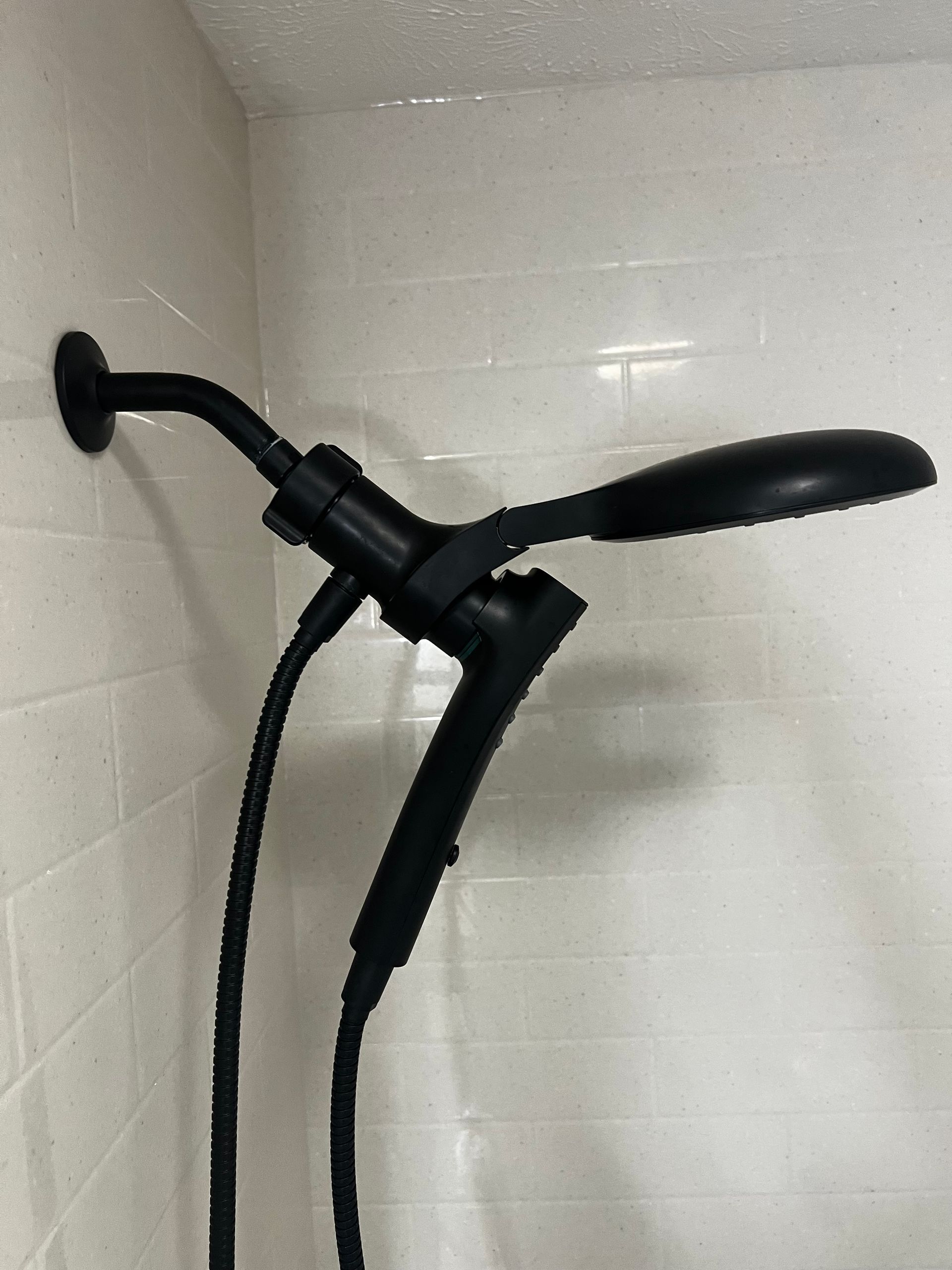 A matte black dual shower head system mounted to a white tiled shower wall.