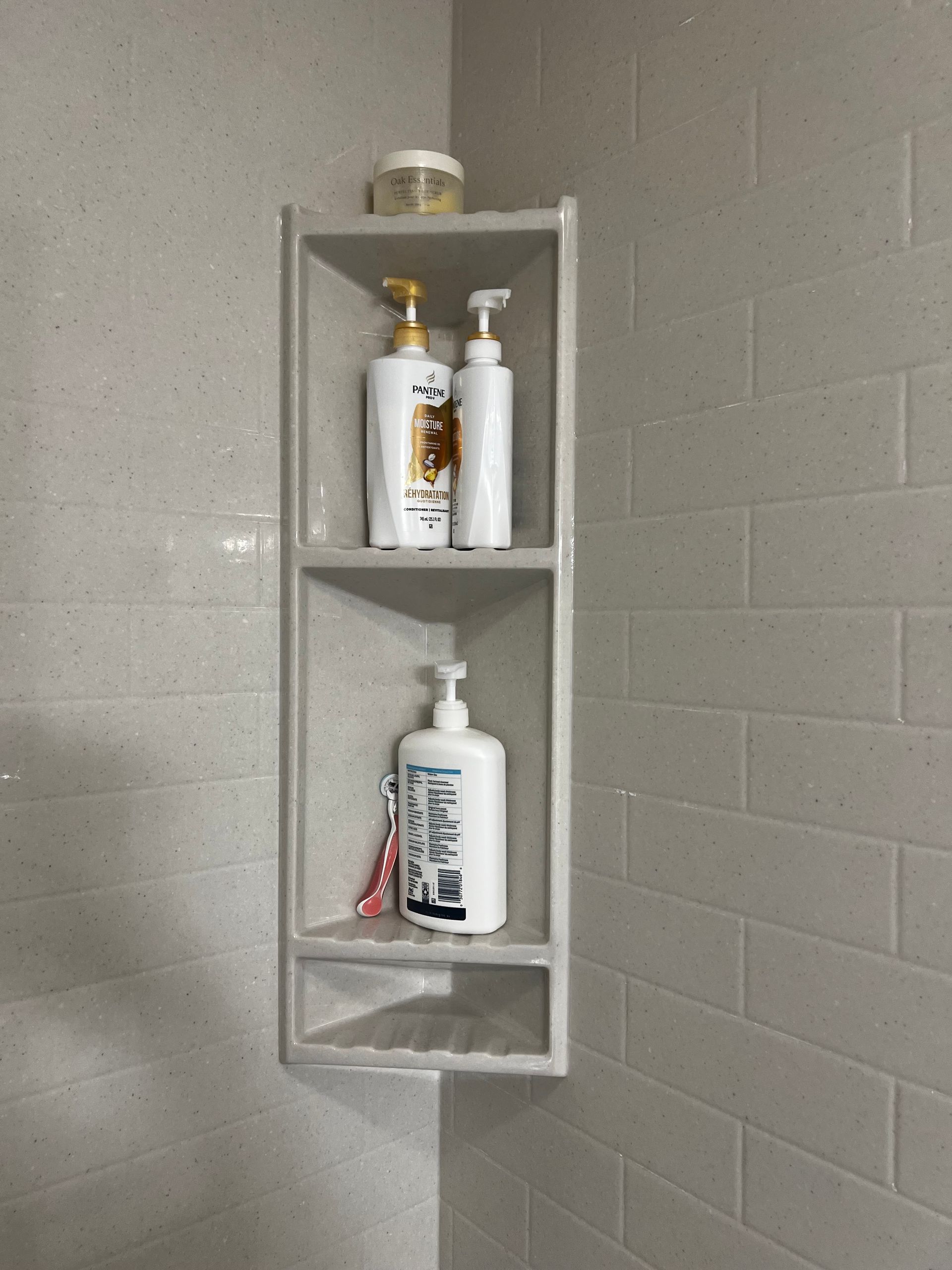 A built-in white corner shower shelf with three tiers holding assorted shampoo and toiletry bottles against tiled walls.