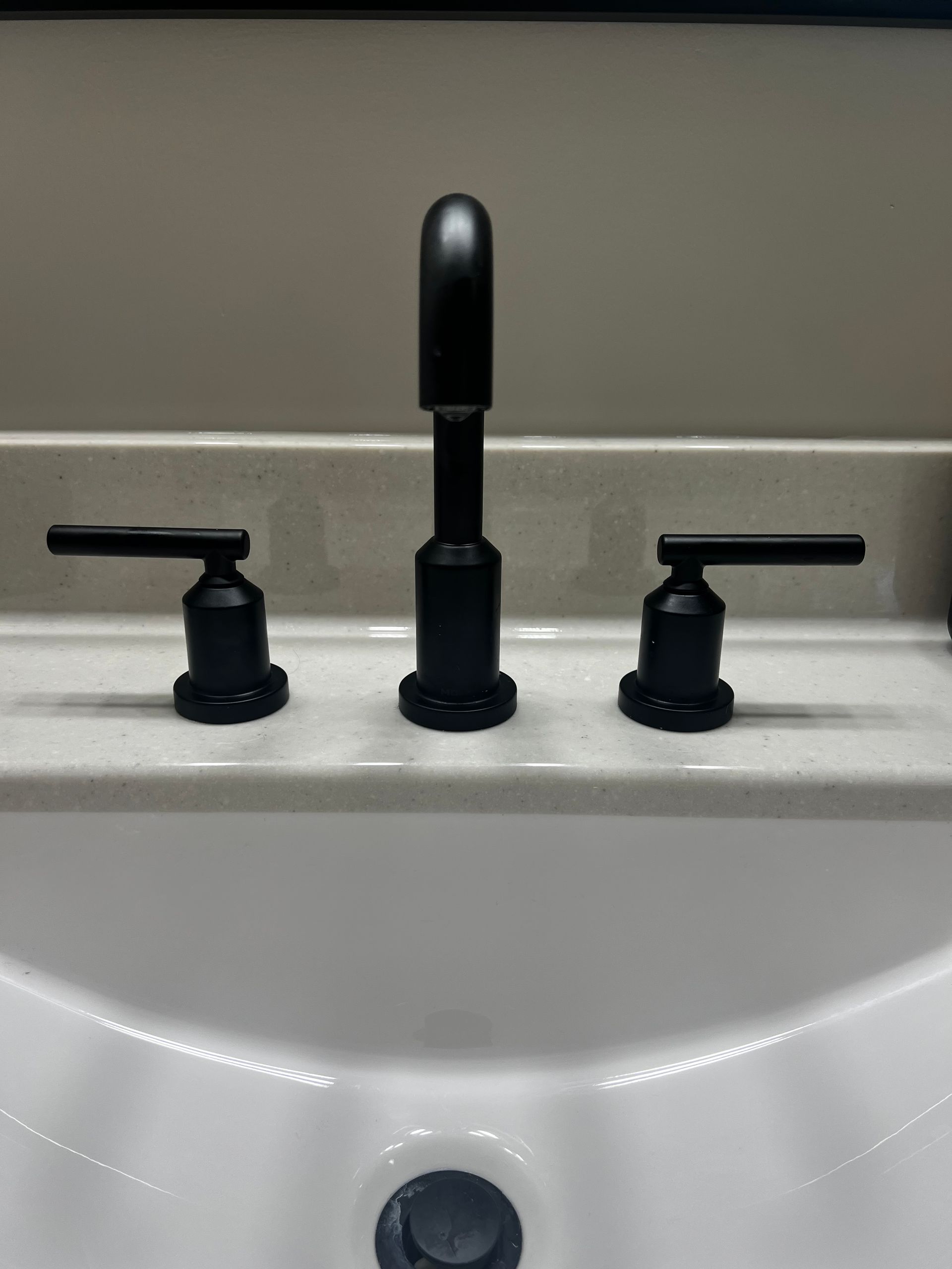 A matte black, three-piece bathroom faucet set centered on a speckled, light-colored stone vanity countertop.