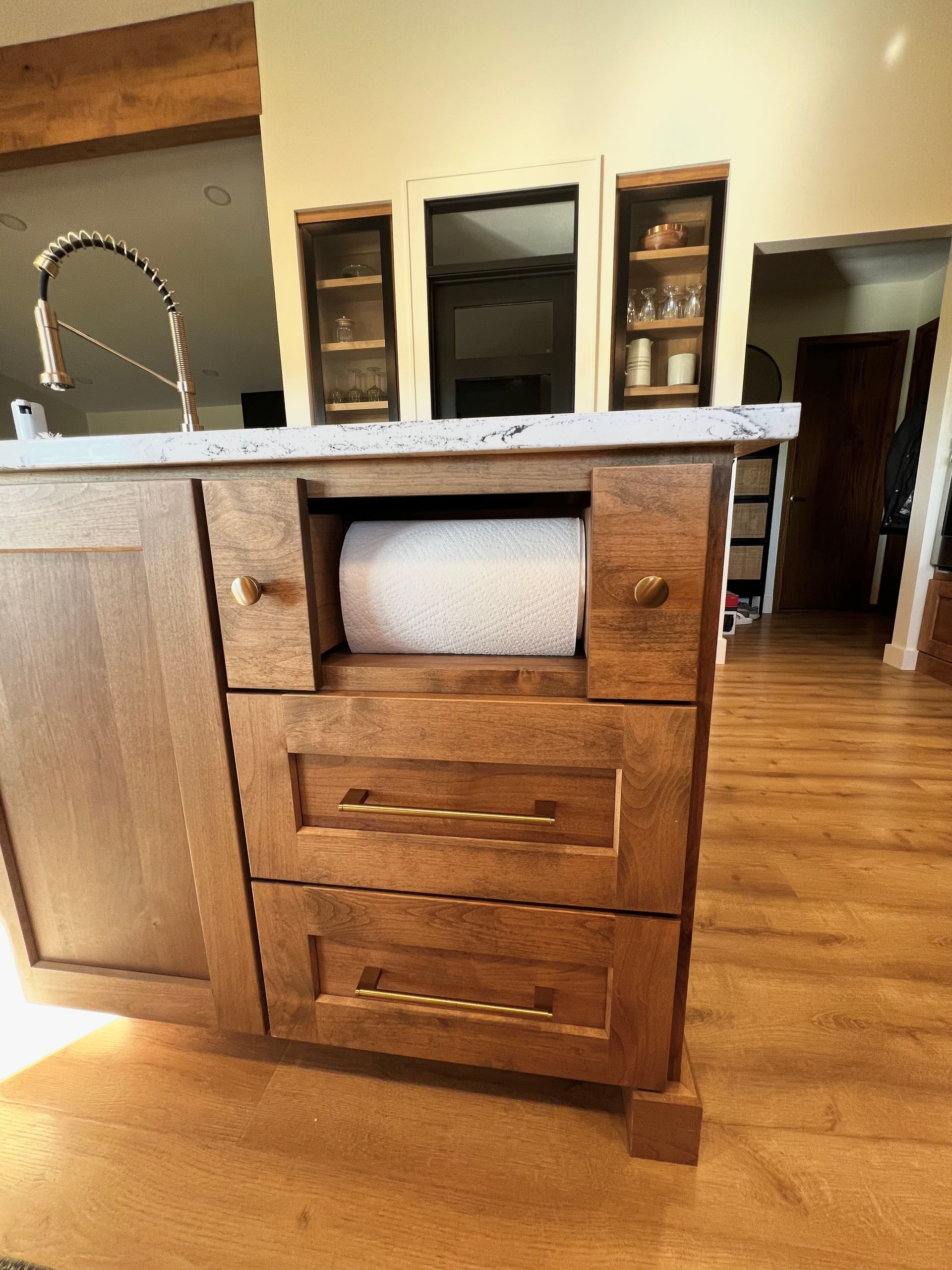 A kitchen island with a built-in paper towel holder above two drawers, finished in stained wood with gold hardware.