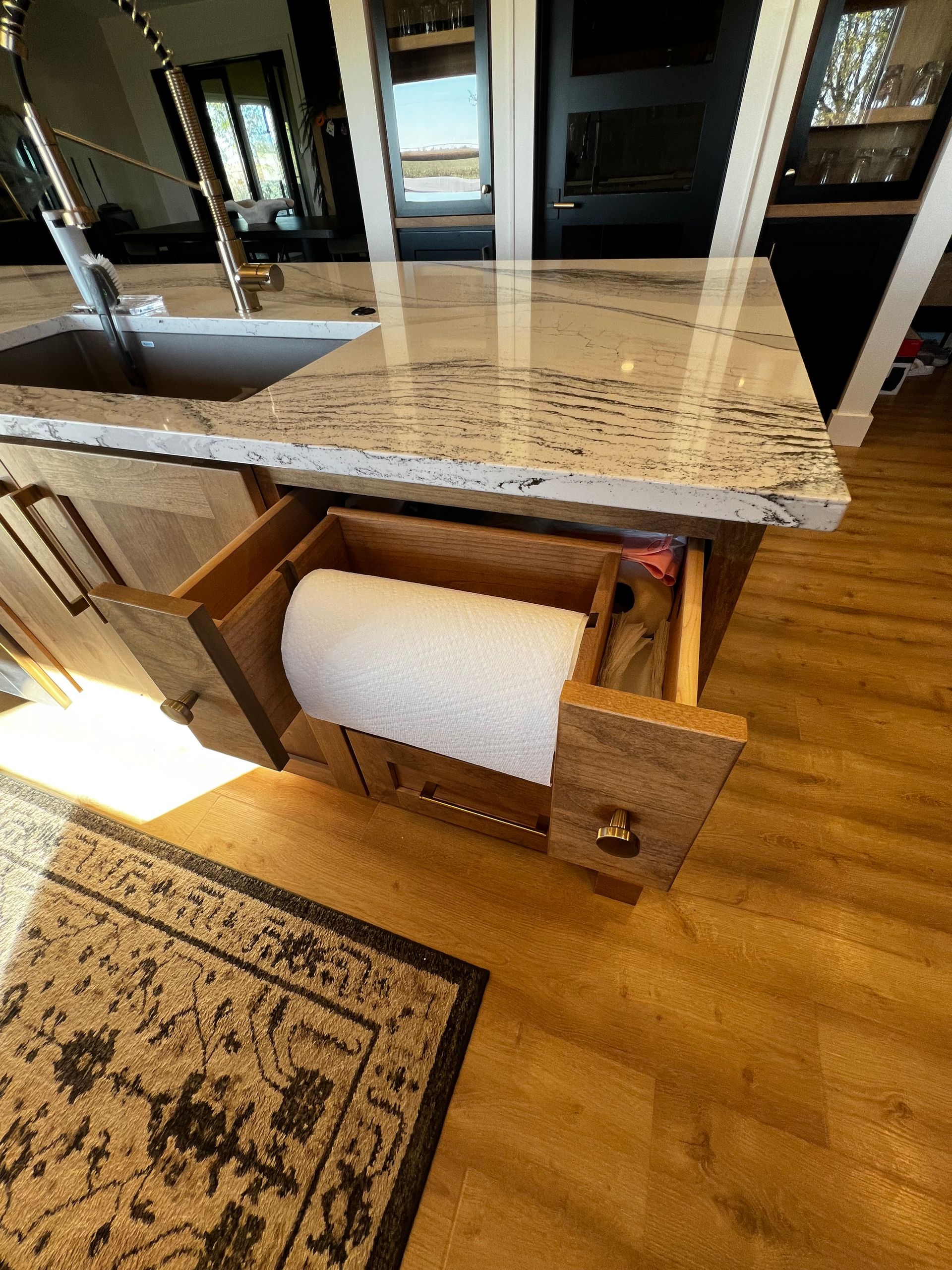 A kitchen island drawer pulled open to reveal a roll of paper towels mounted horizontally inside the cabinet.