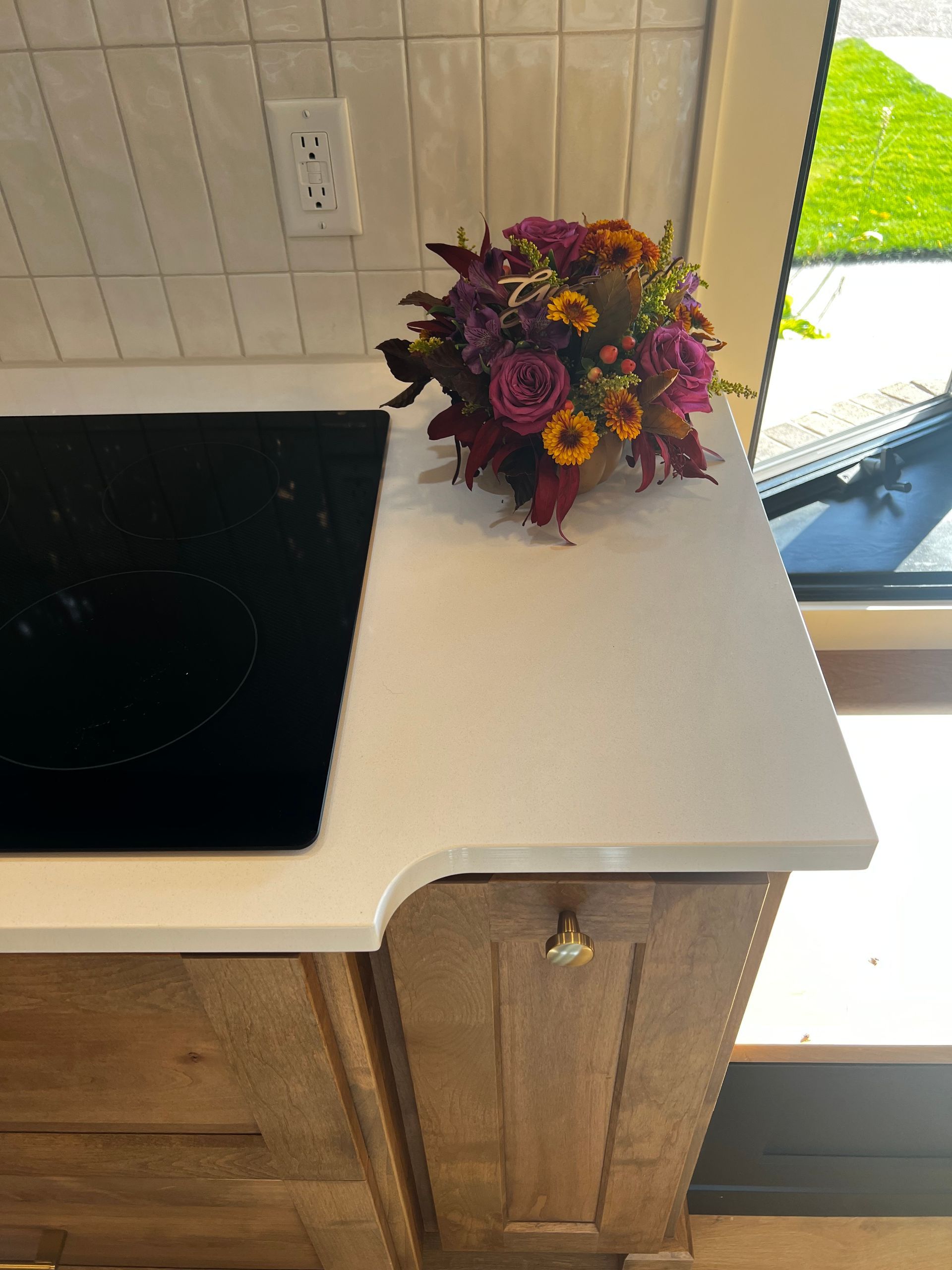 A small bouquet of purple and orange flowers sits on a white kitchen counter next to a black induction cooktop.